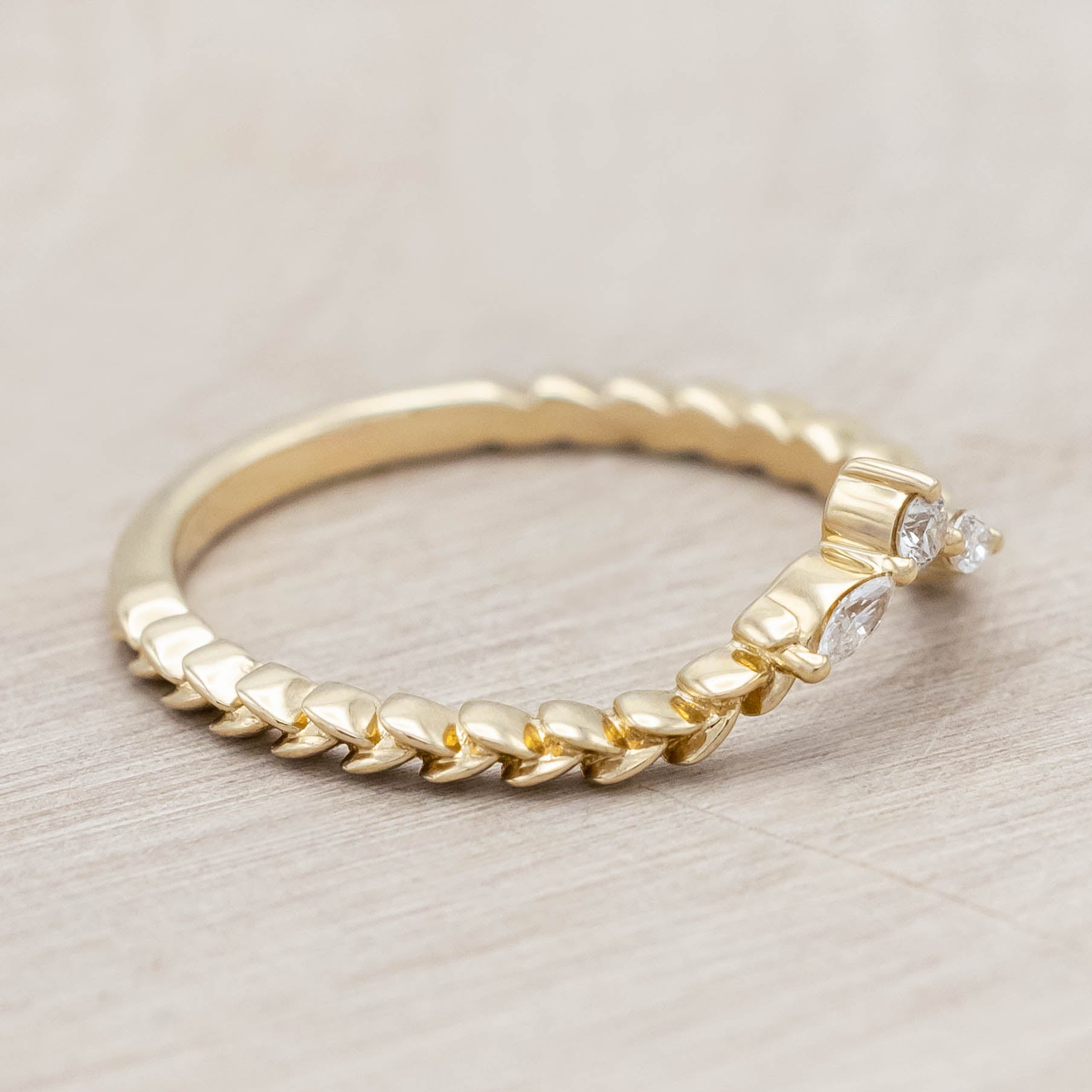 14K gold ring with three diamonds on a wooden stand against a beige background