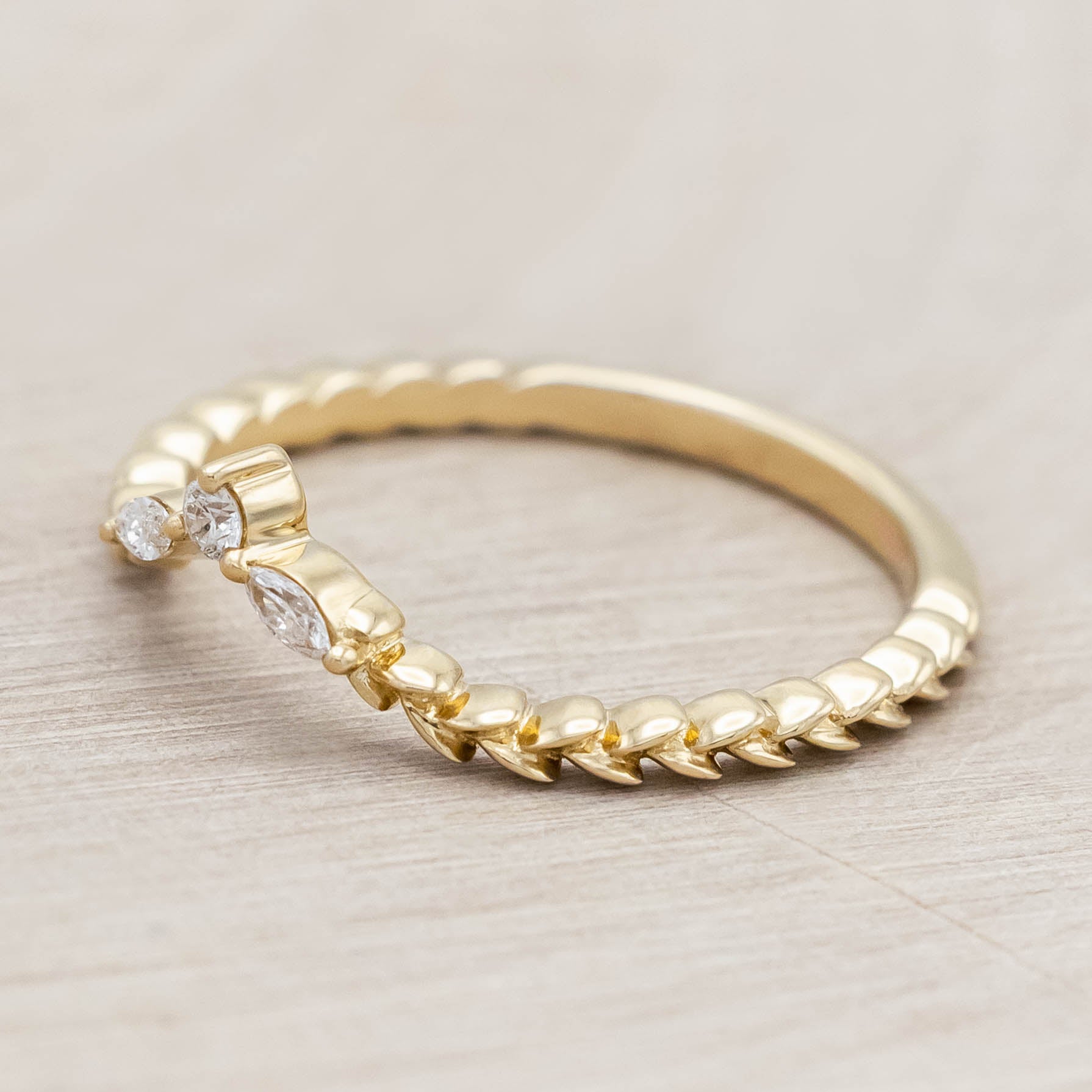 14K gold ring with three diamonds on a wooden stand against a beige background