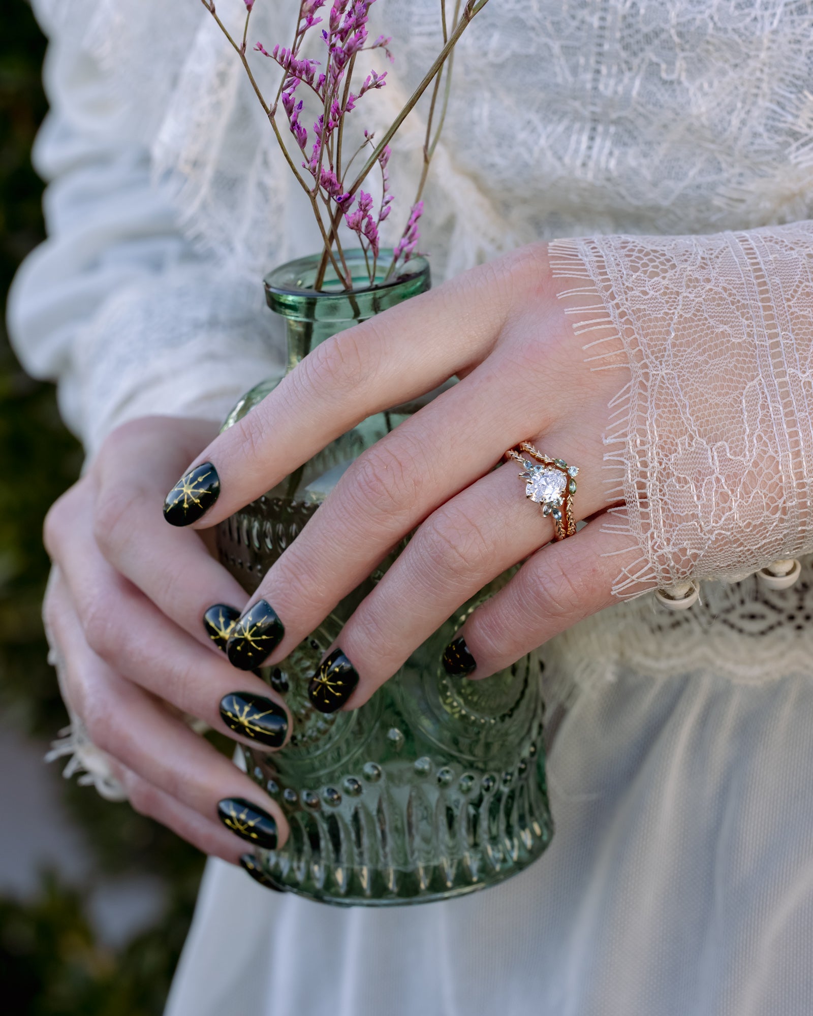 Person holding a small green vase with pink flowers, wearing a gold ring with a diamond.