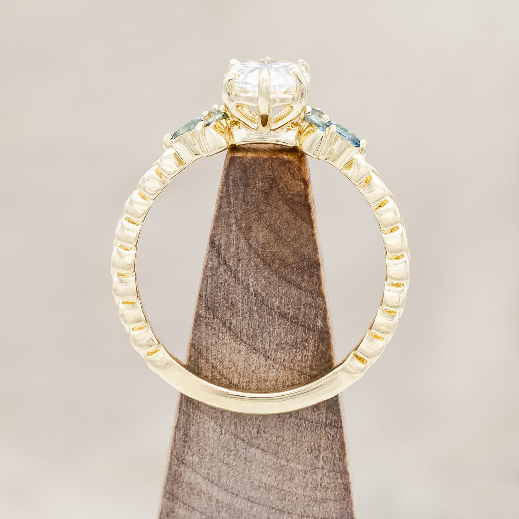 Gold ring with lab diamond centerstone, tourmaline and sapphire accents on a beige background