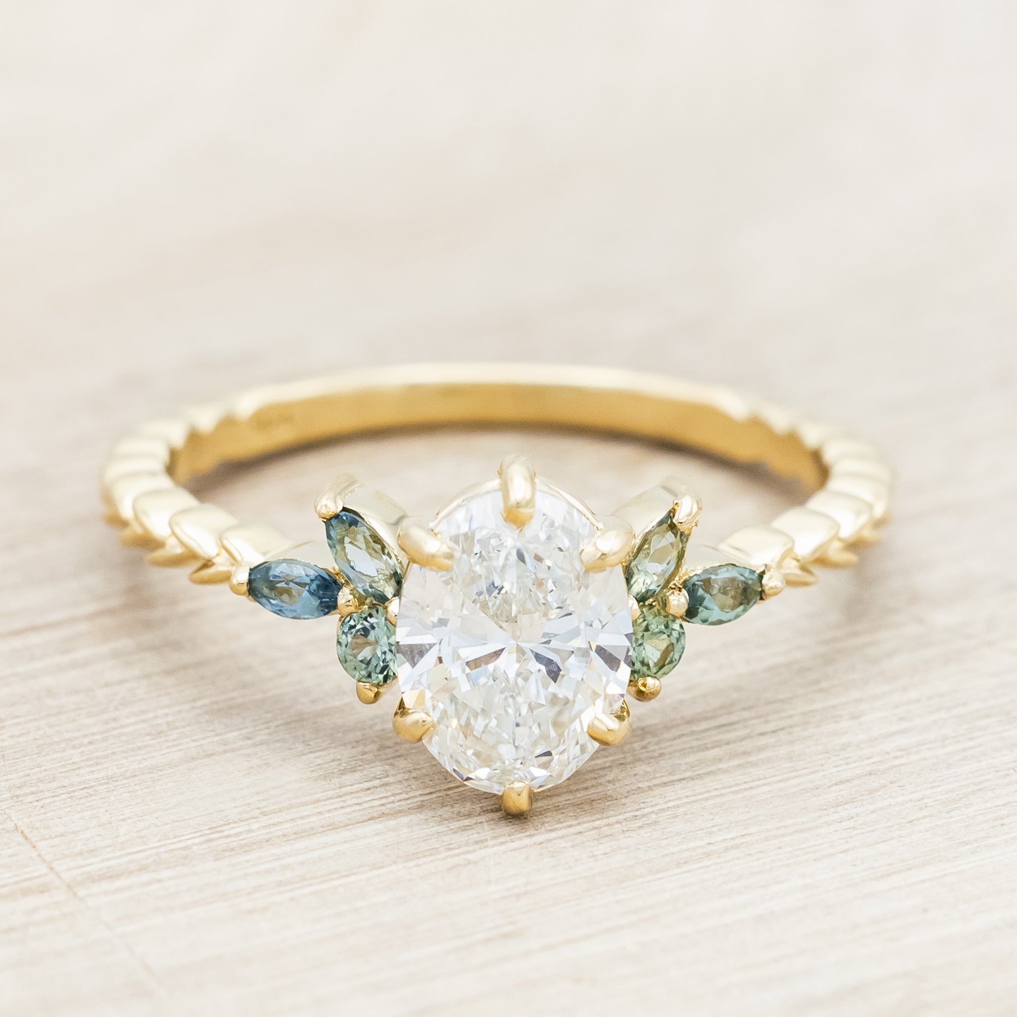 Gold ring with lab diamond centerstone, tourmaline and sapphire accents on a beige background
