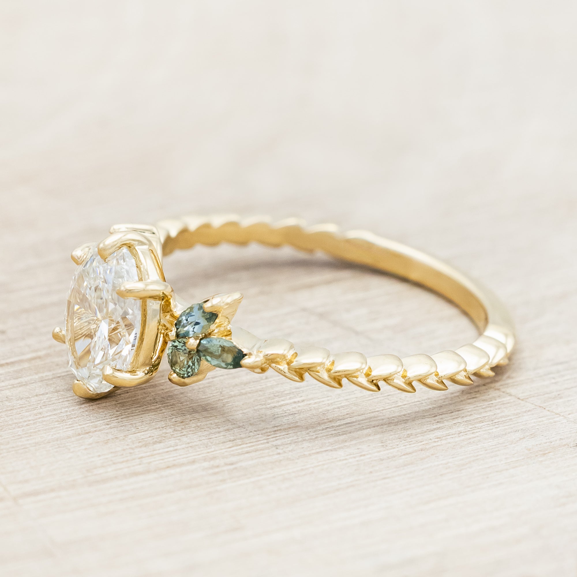 Gold ring with lab diamond centerstone, tourmaline and sapphire accents on a beige background