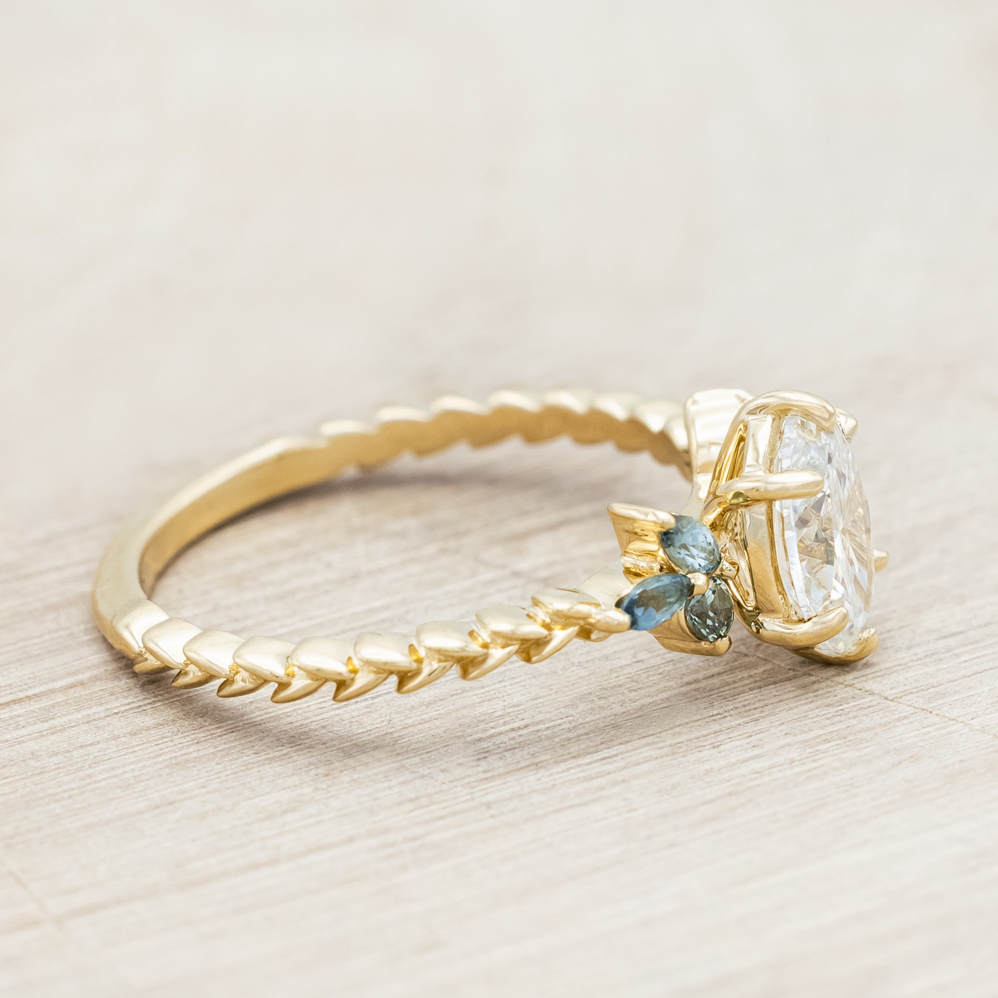 Gold ring with lab diamond centerstone, tourmaline and sapphire accents on a beige background