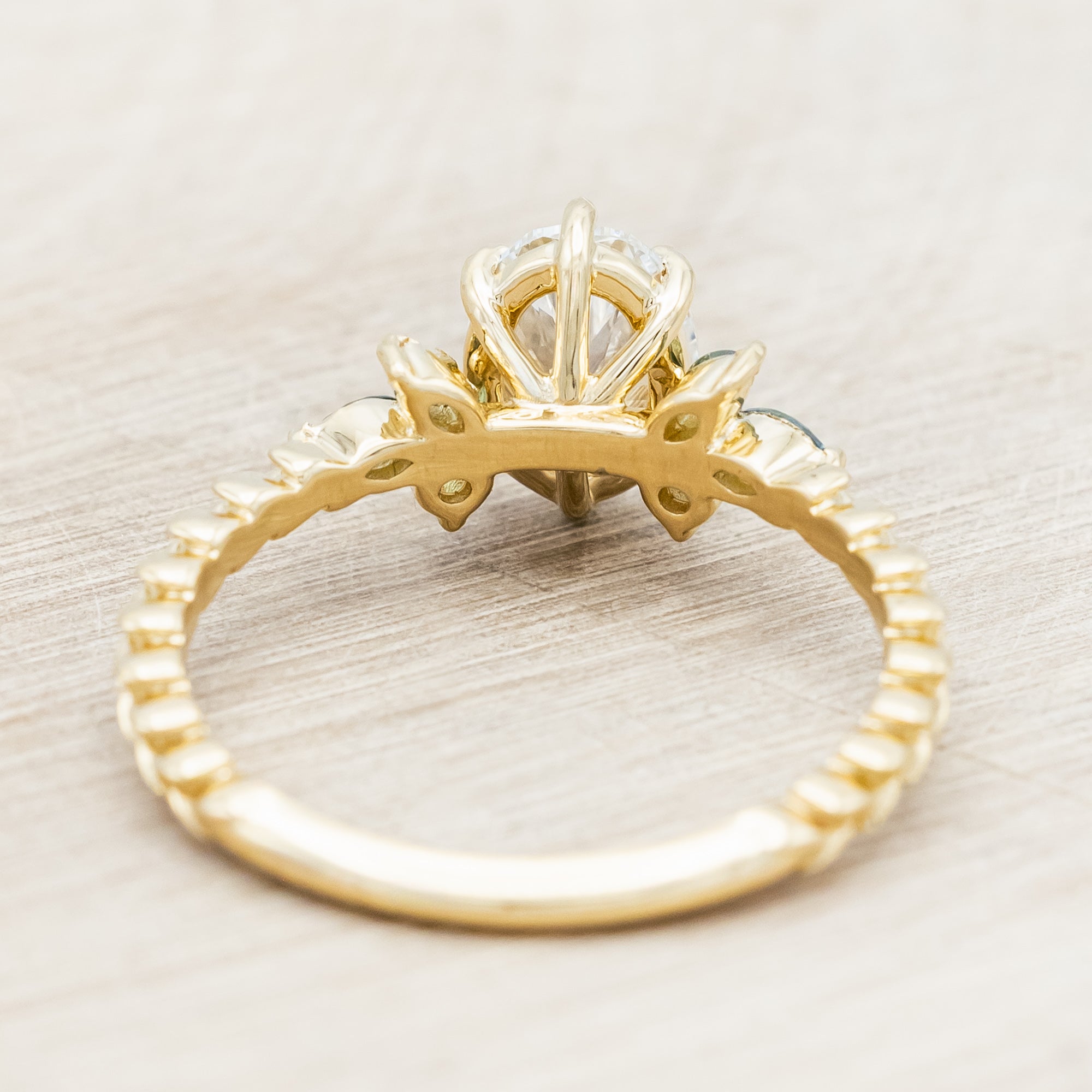Gold ring with lab diamond centerstone, tourmaline and sapphire accents on a beige background