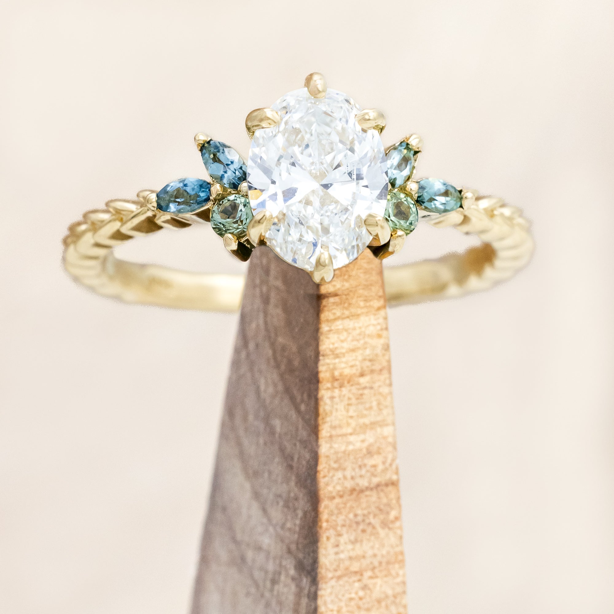 Gold ring with lab diamond centerstone, tourmaline and sapphire accents on a beige background