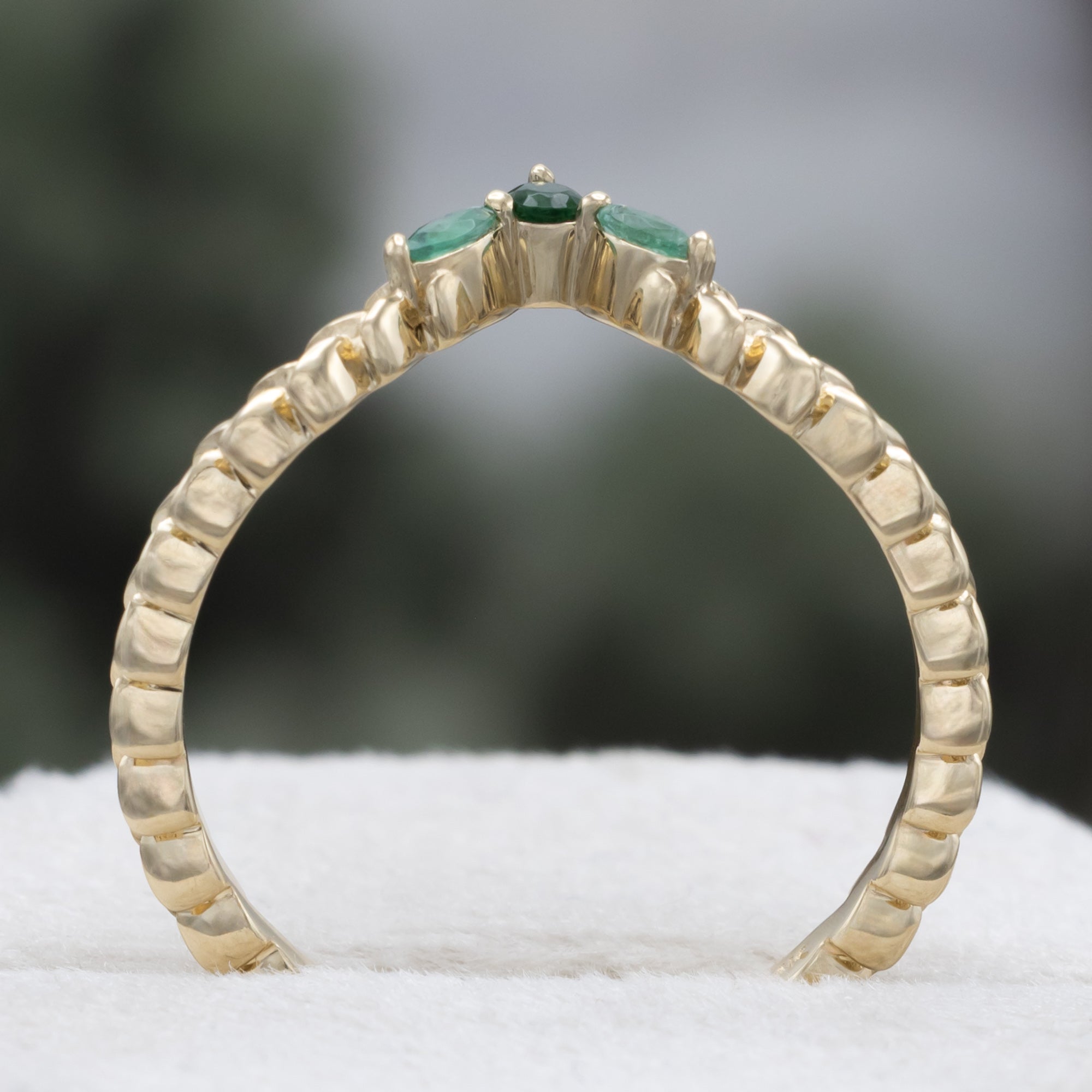 A close-up of a gold tracer with a multiple green emerald accents against a blurred natural background.