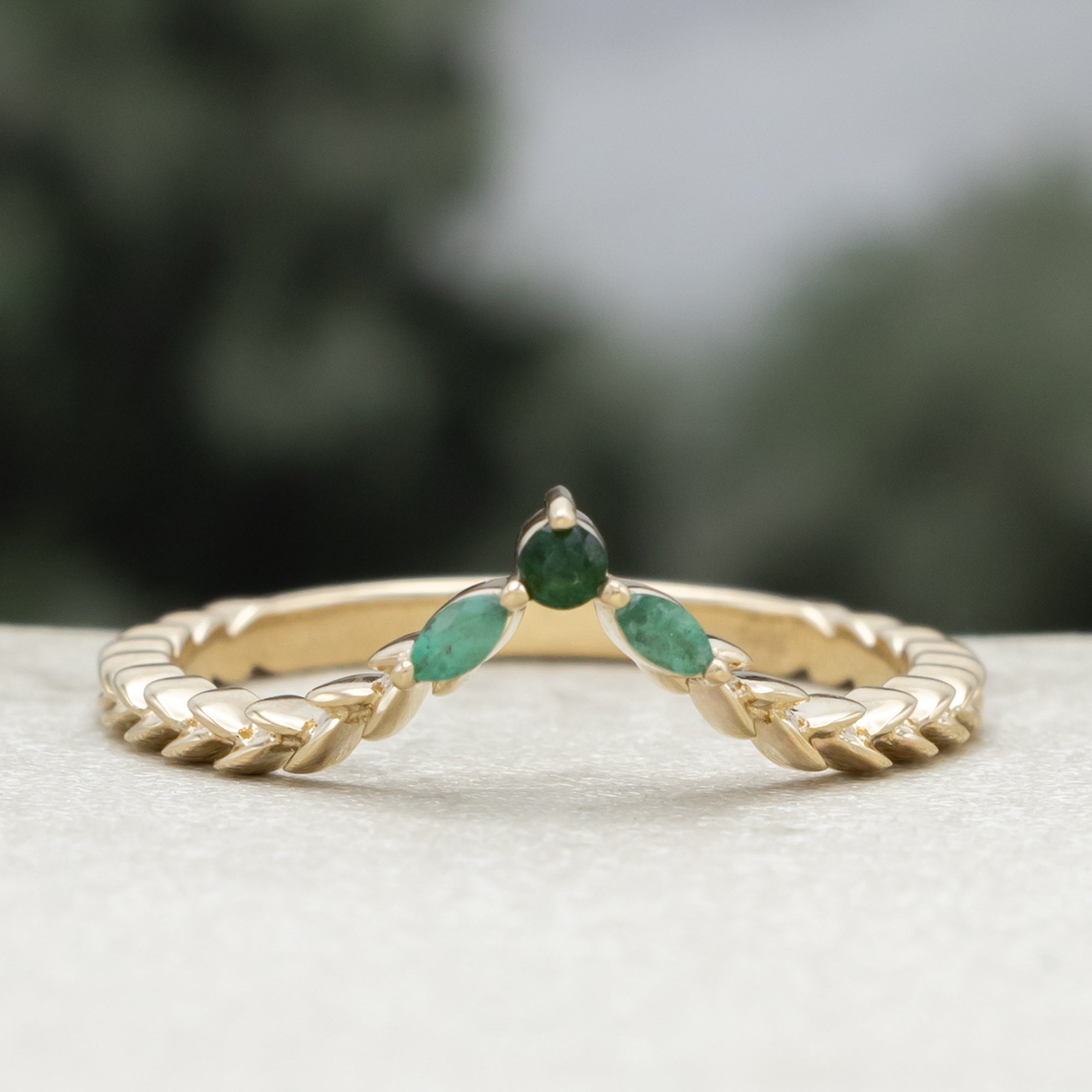 A close-up of a gold tracer with a multiple green emerald accents against a blurred natural background.