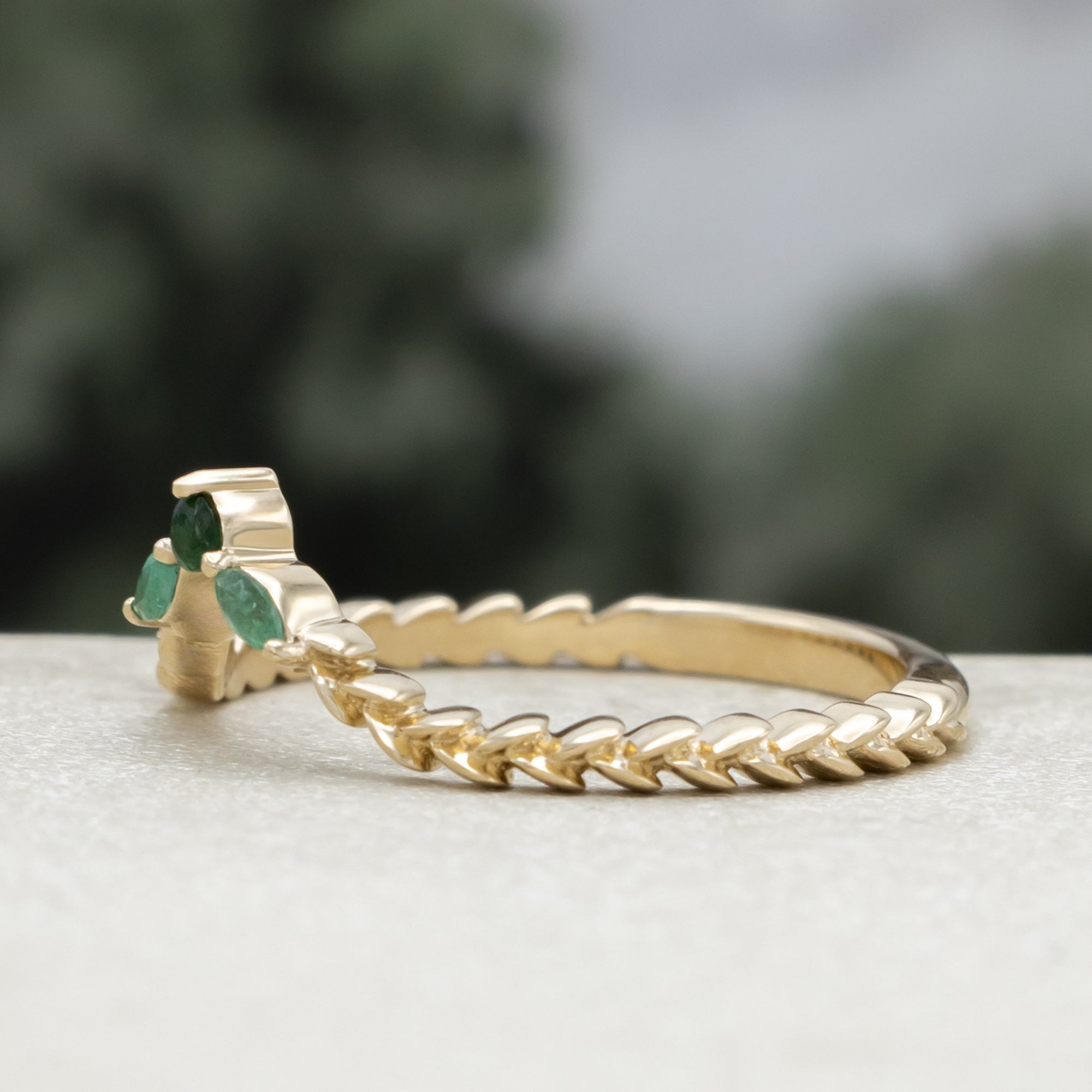 A close-up of a gold tracer with a multiple green emerald accents against a blurred natural background.