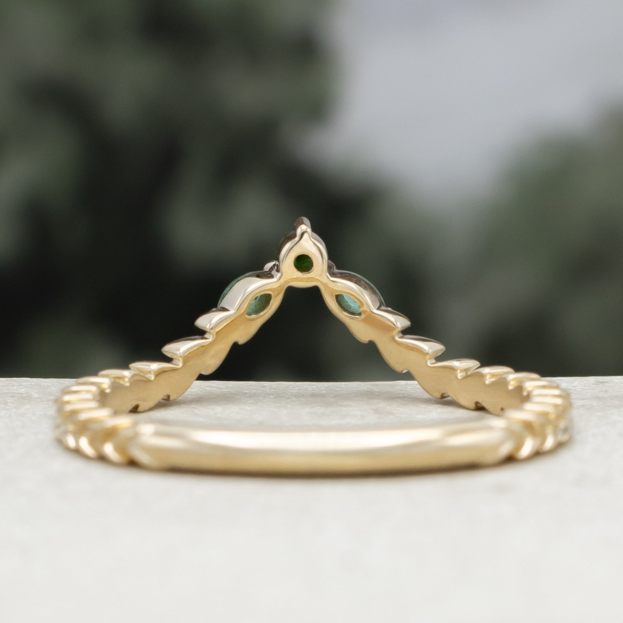 A close-up of a gold tracer with a multiple green emerald accents against a blurred natural background.