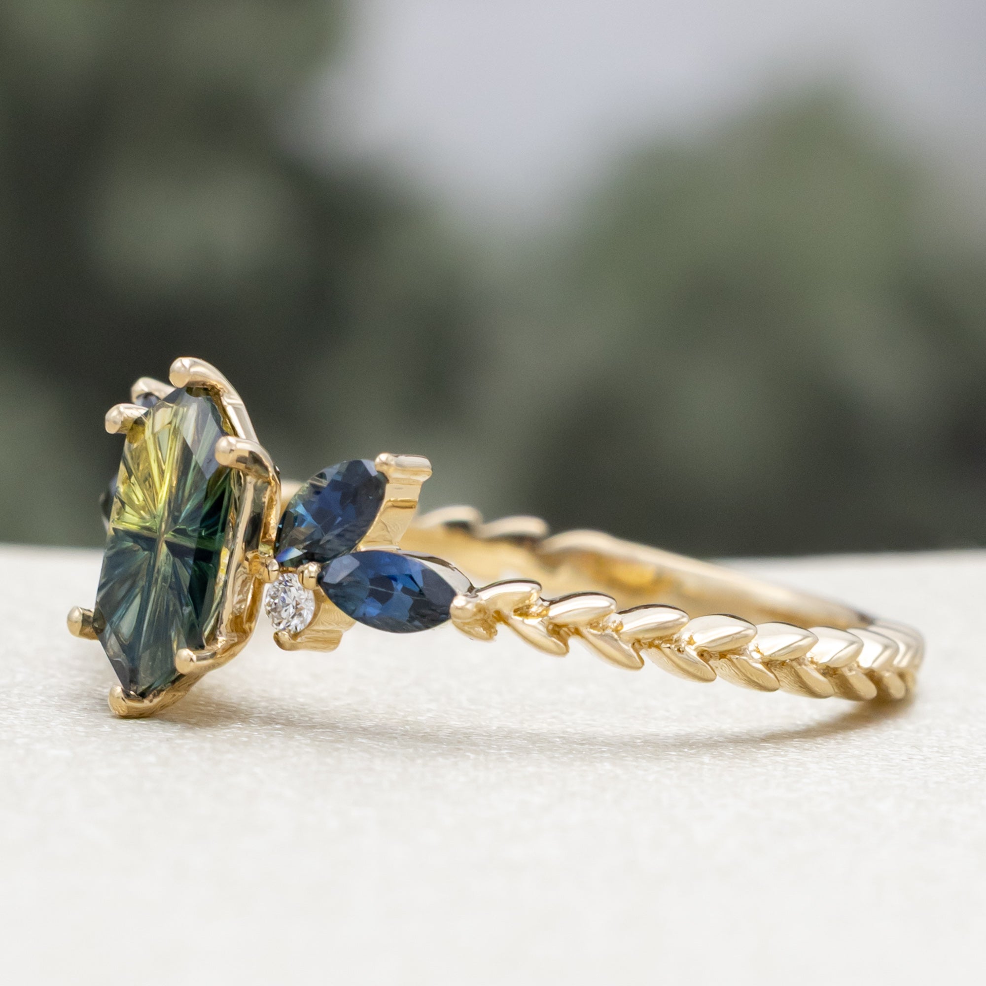 Gold ring with Australian sapphire center stone and diamond accents on a blurred background