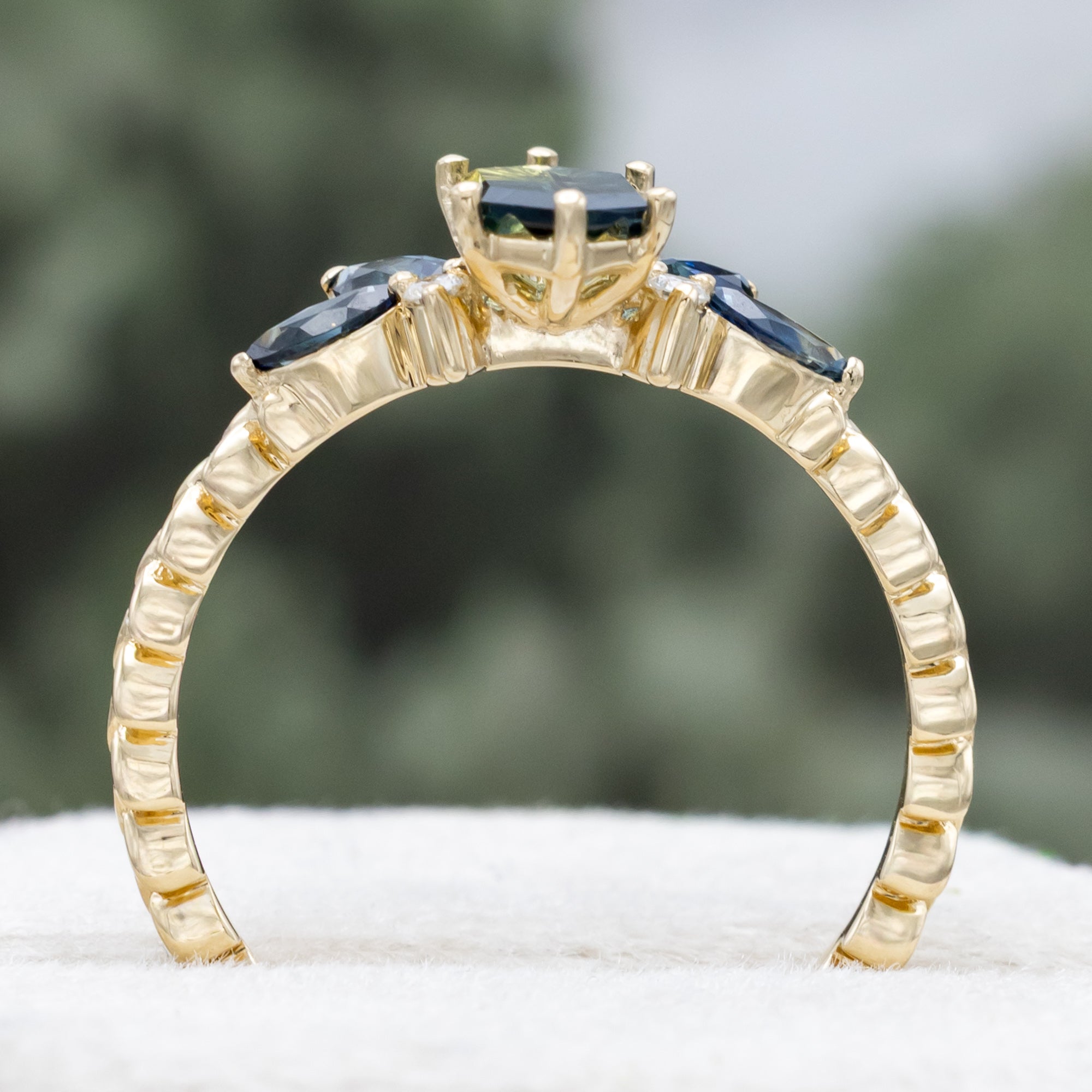 Gold ring with Australian sapphire center stone and diamond accents on a blurred background