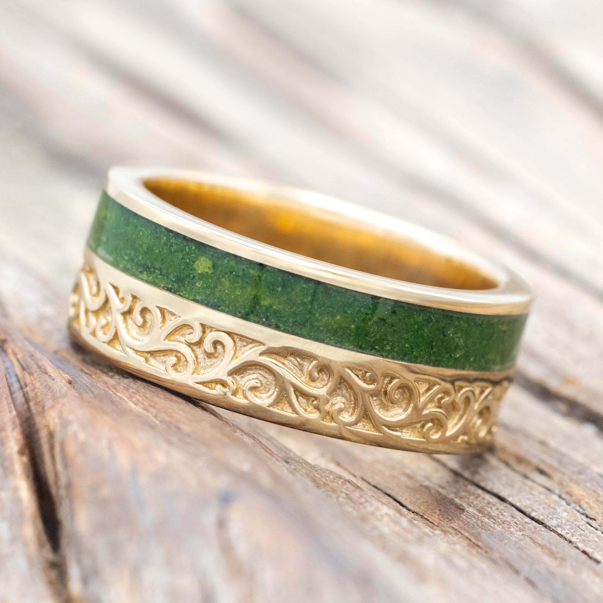 Yellow gold ring with vine engraving and moss inlay on a wooden background