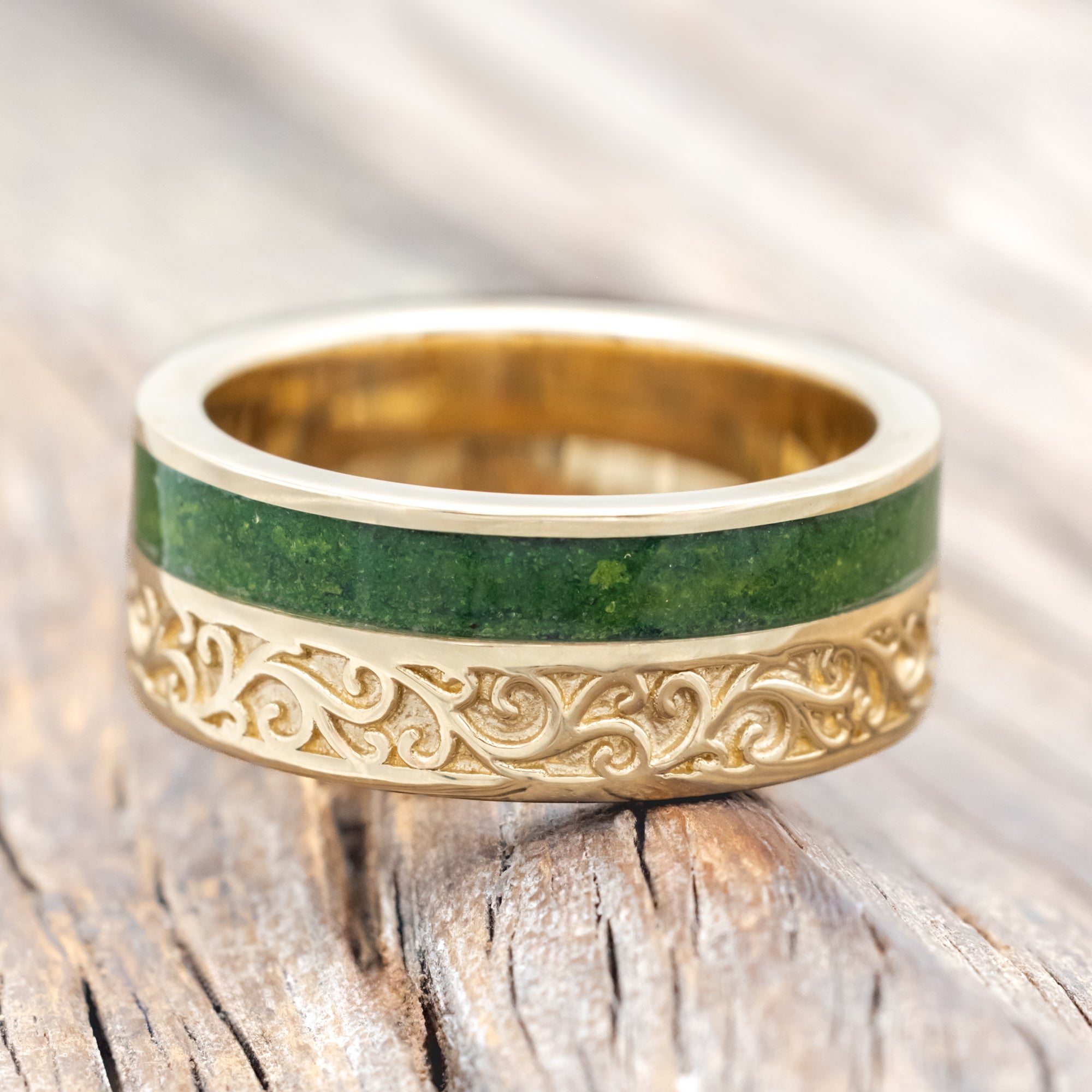 Yellow gold ring with vine engraving and moss inlay on a wooden background