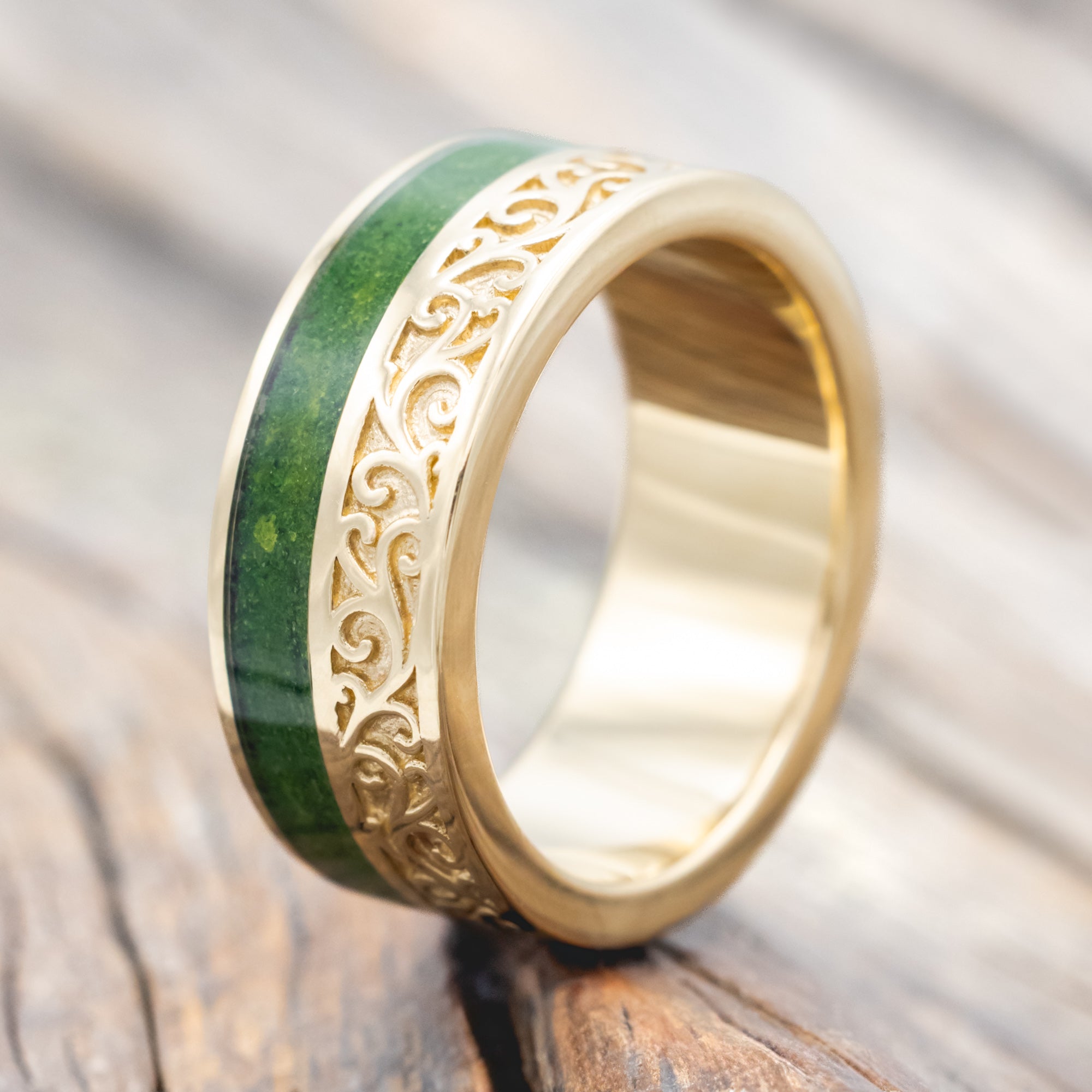 Yellow gold ring with vine engraving and moss inlay on a wooden background
