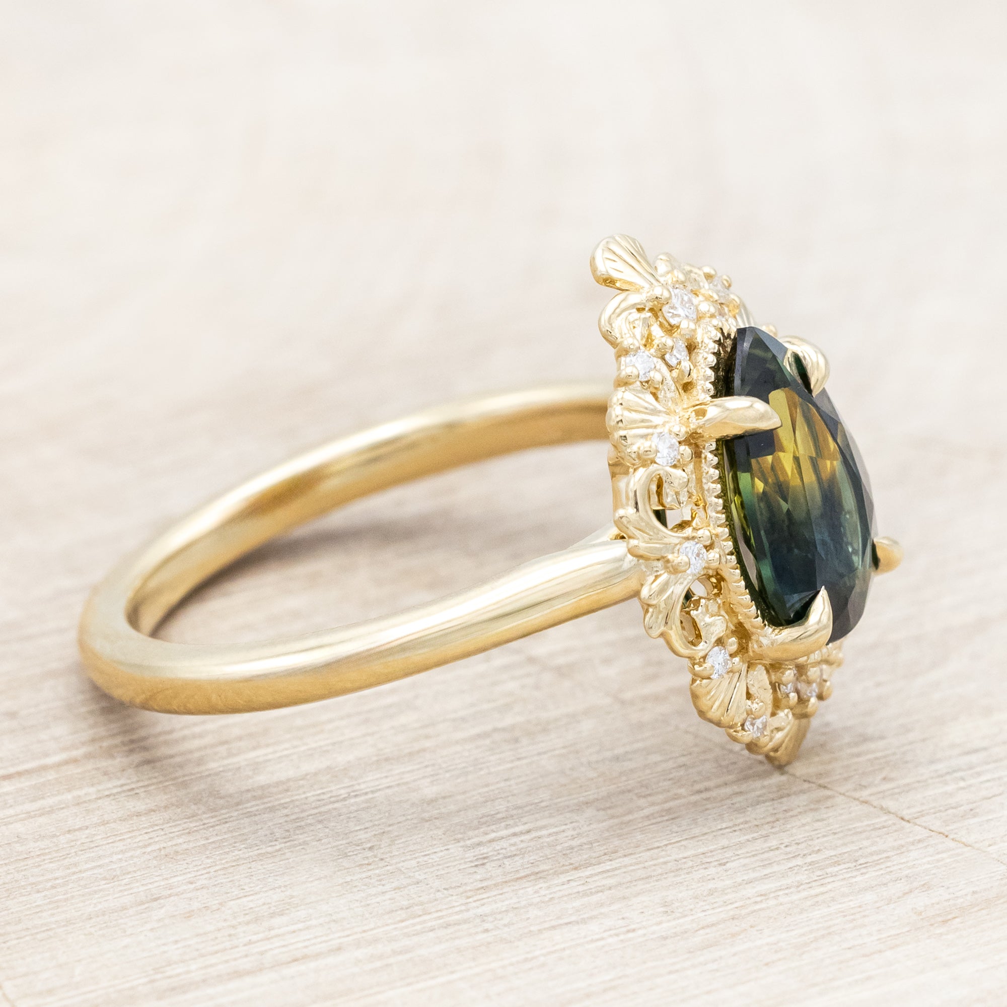 Gold ring with a green sapphire on a light wooden surface