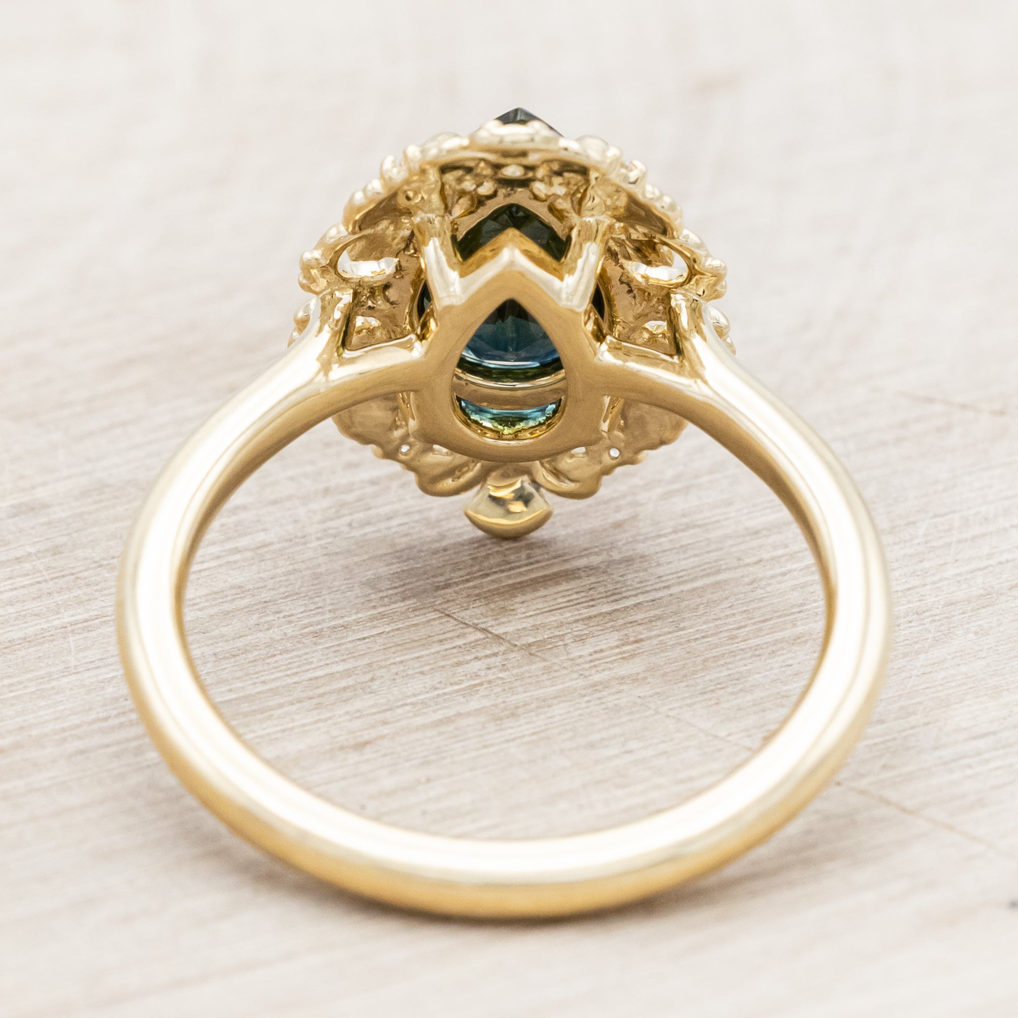 Gold ring with a green sapphire on a light wooden surface