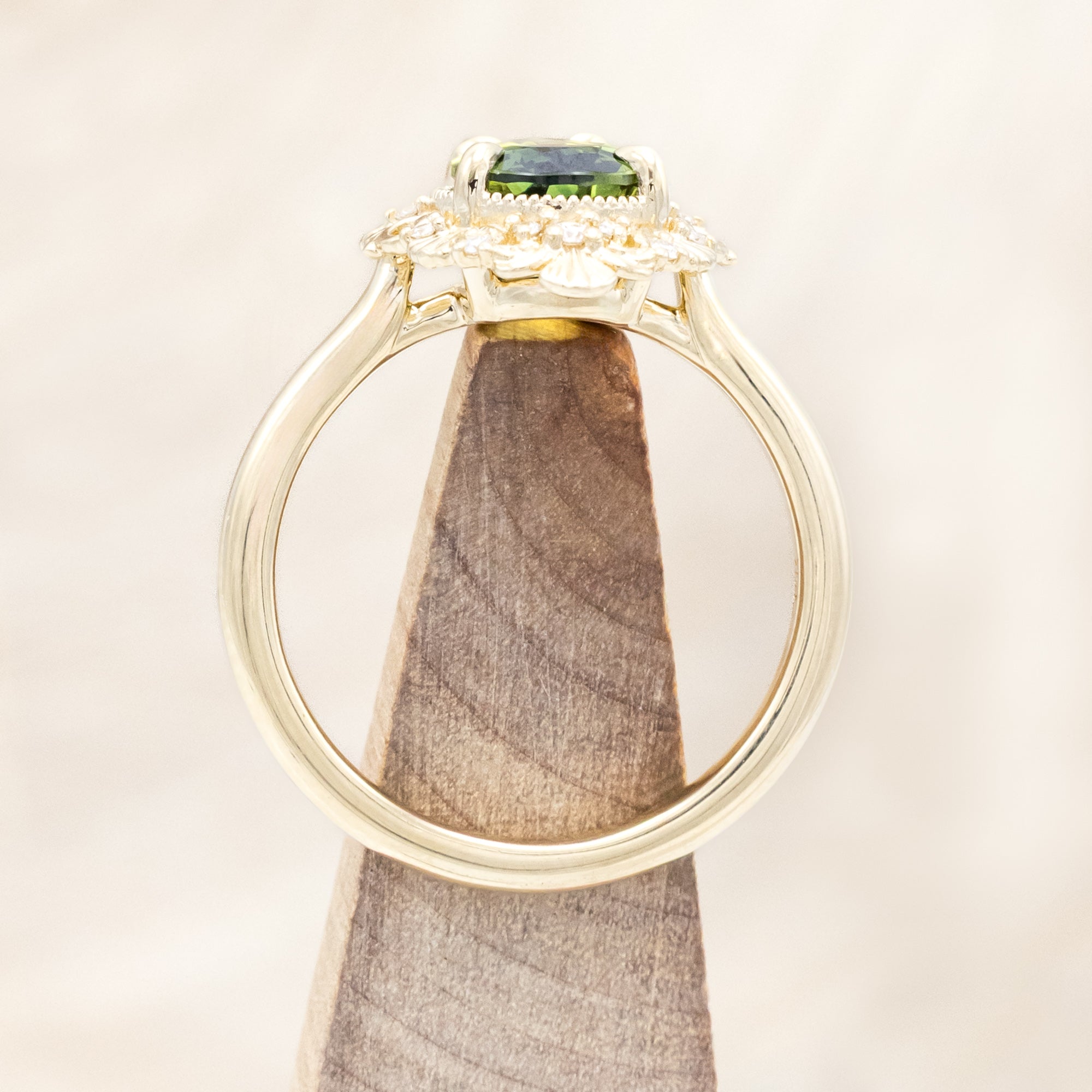 Gold ring with a green sapphire on a beige background