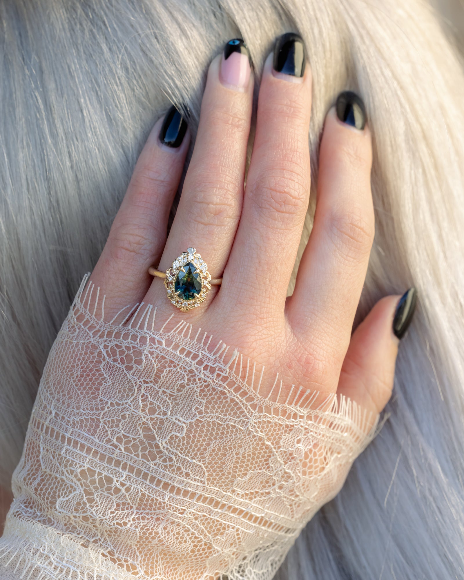 Hand wearing a ring and lace sleeve with a green sapphire against a neutral background