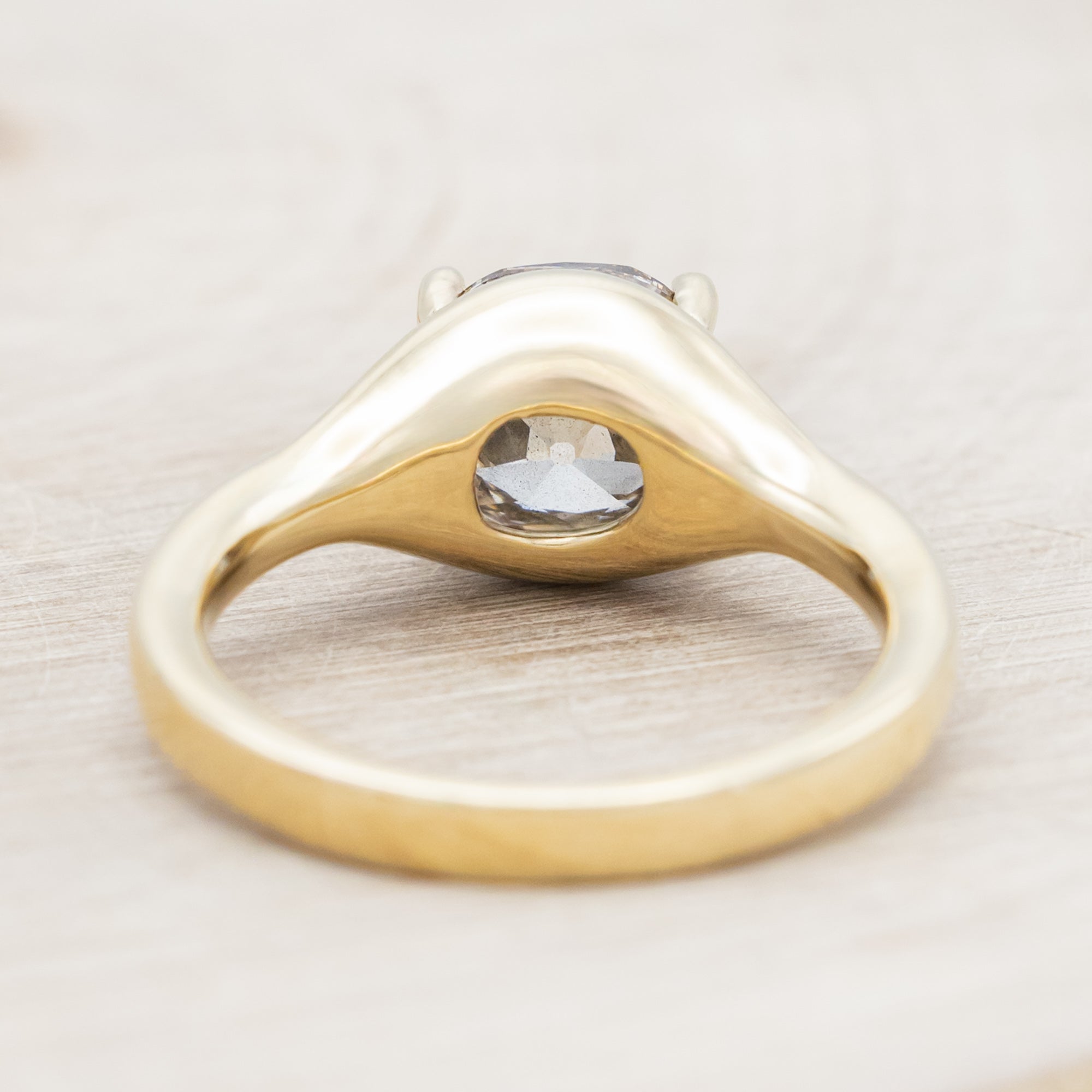 Gold ring with a large salt & pepper diamond on a light wooden surface