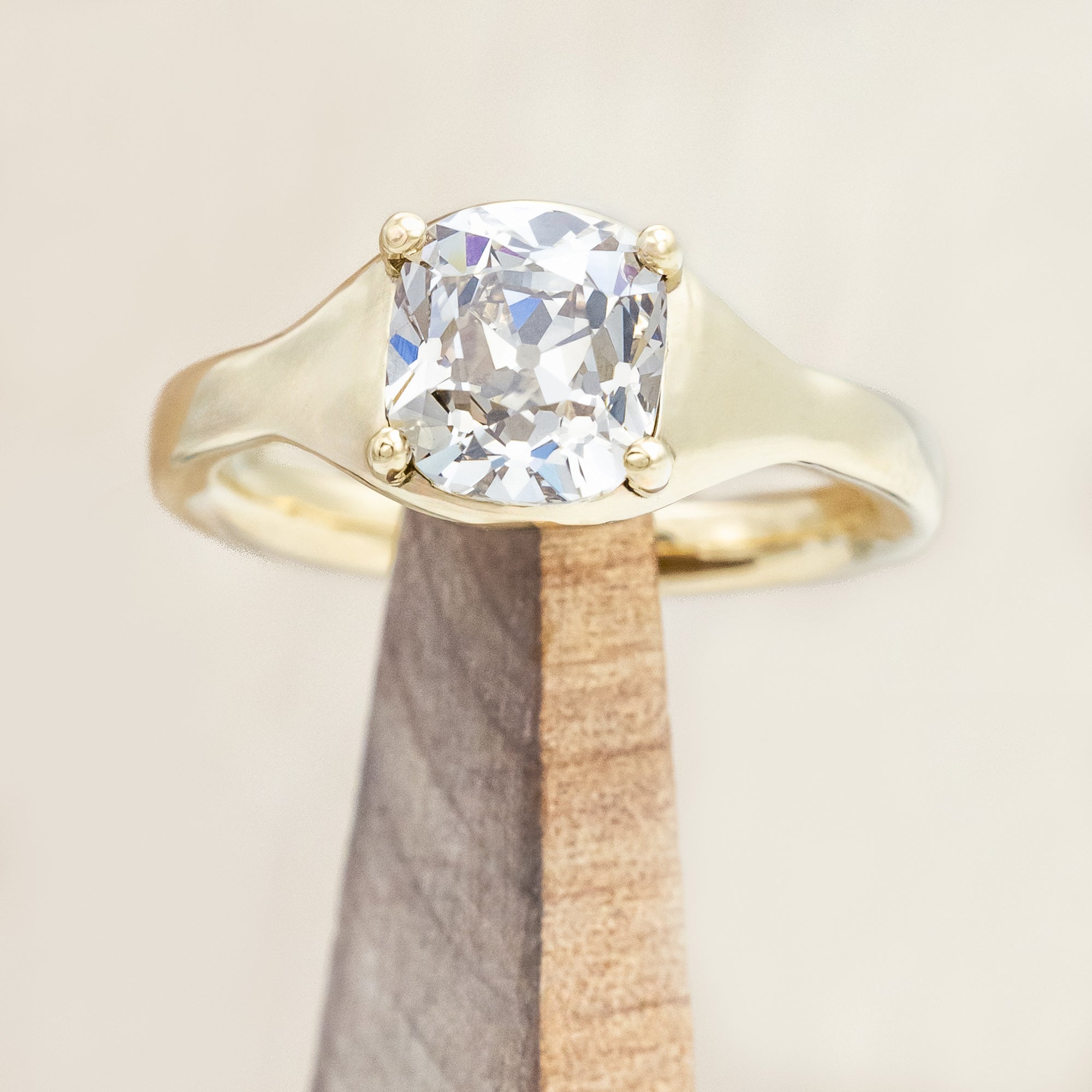 Gold ring with a large salt & pepper diamond on a wooden stand against a beige background