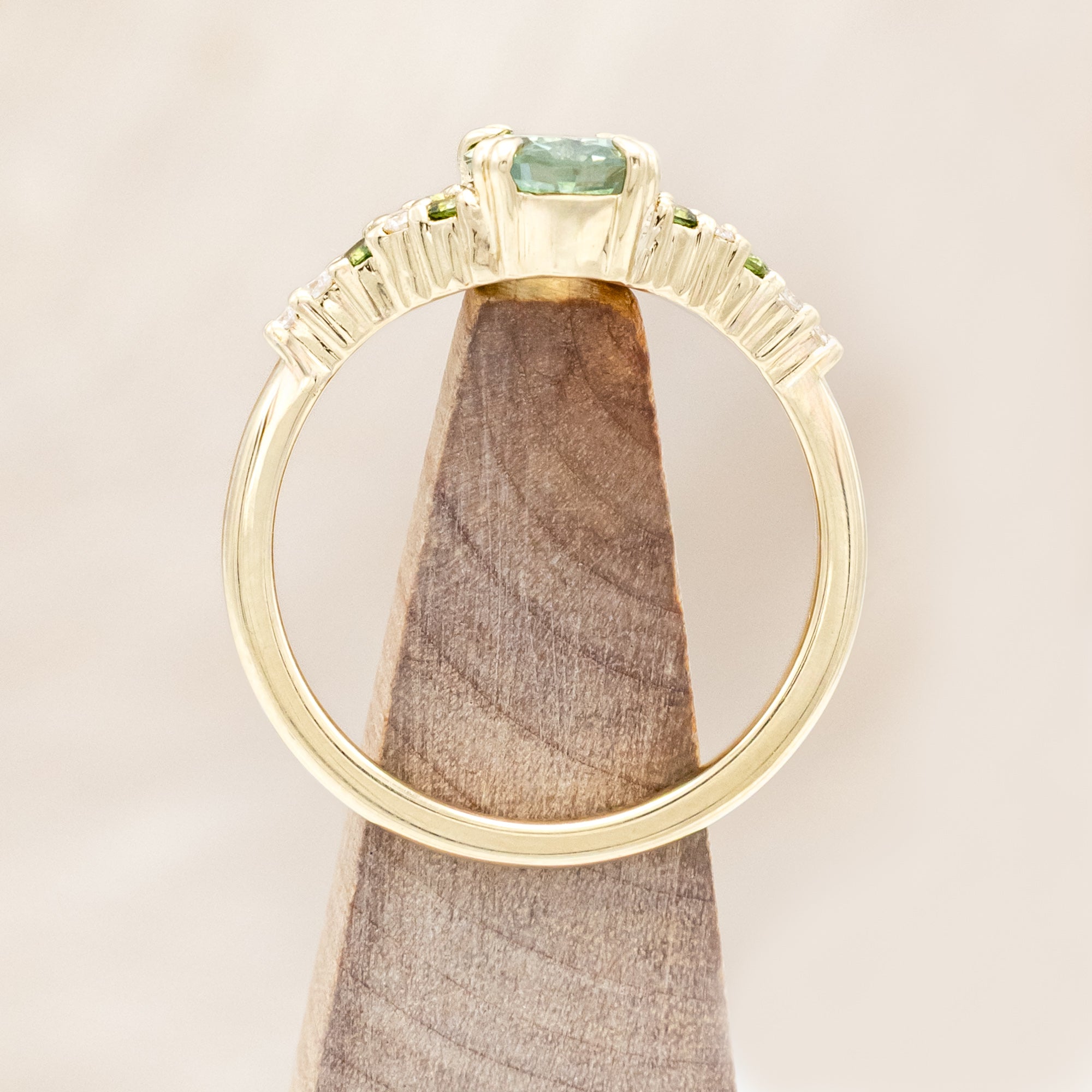 Gold ring with green sapphire and diamond accents on a light wooden surface