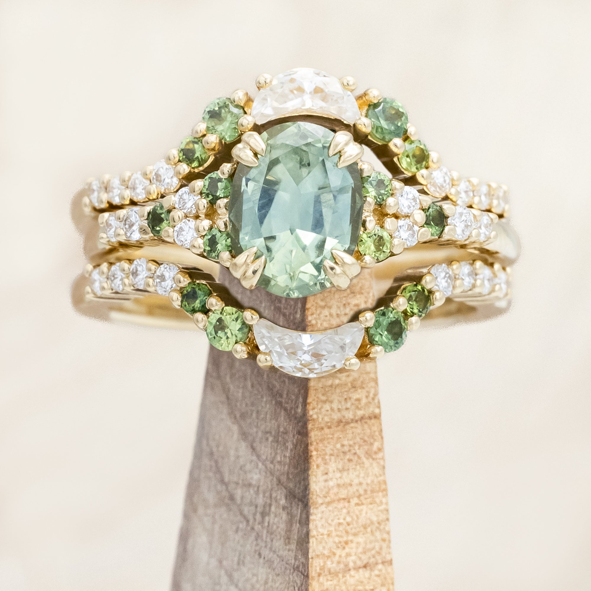 Gold ring with green sapphire and diamond accents on a wooden stand.