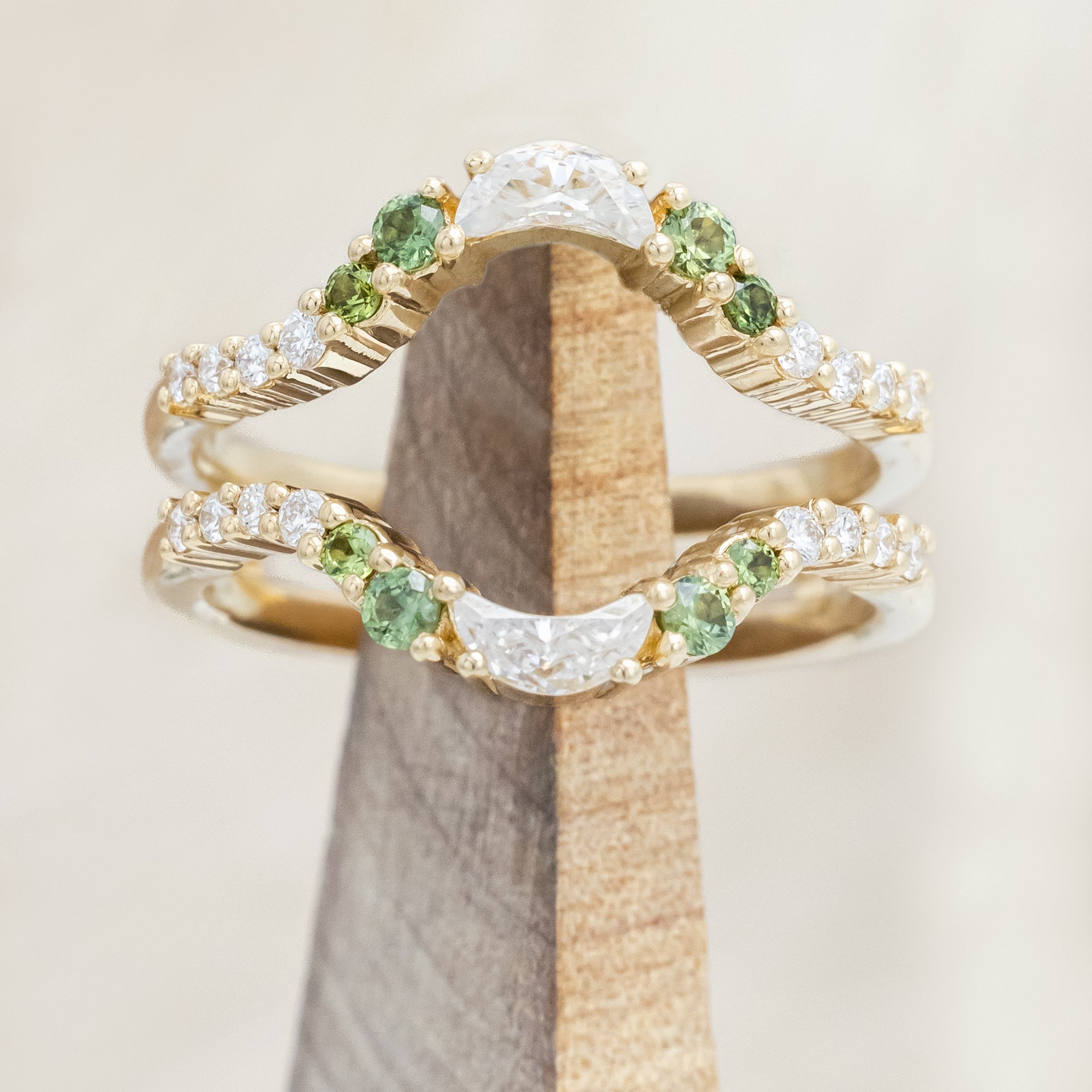 Gold ring with moissanite, green sapphire & diamond accemts on a wooden stand against a beige background