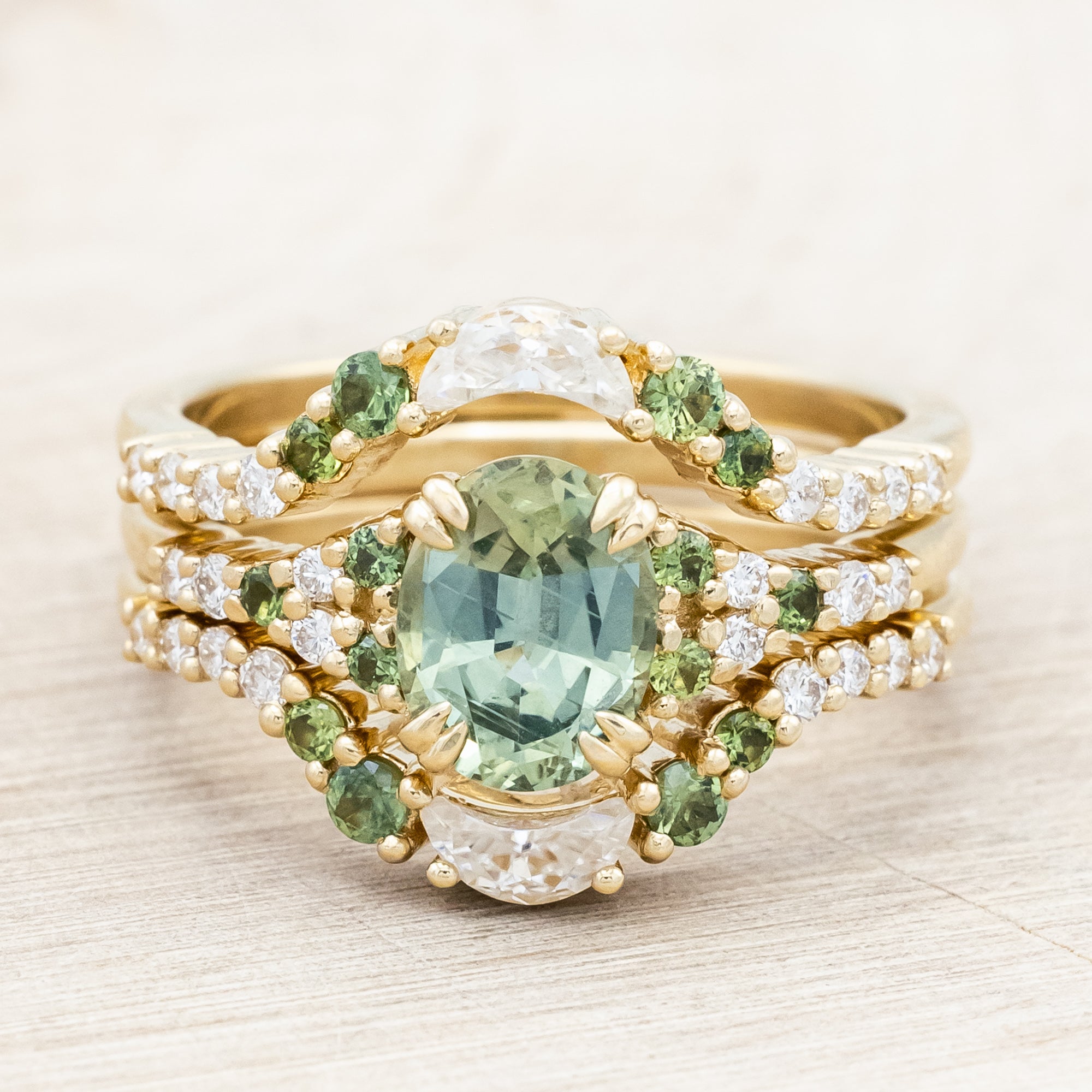 Gold ring with green sapphire and diamond accents on a light wooden surface