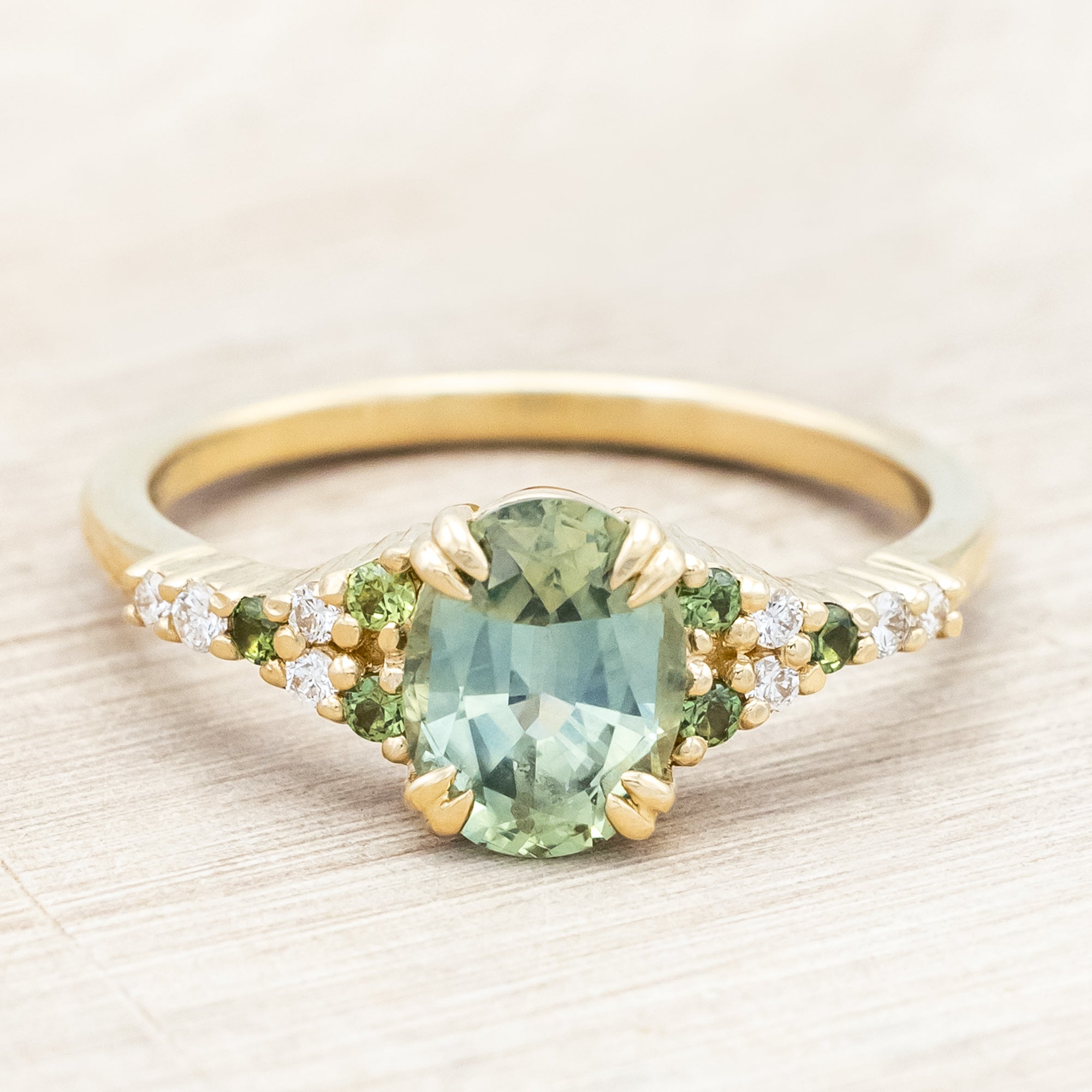 Gold ring with green sapphire and diamond accents on a light wooden surface
