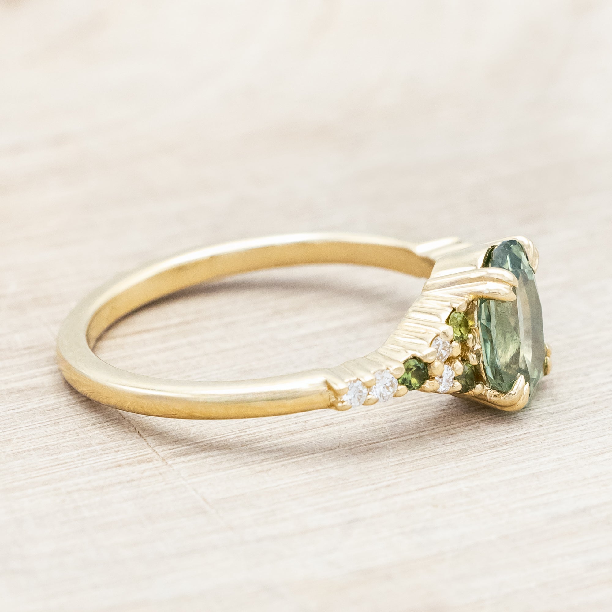 Gold ring with green sapphire and diamond accents on a light wooden surface