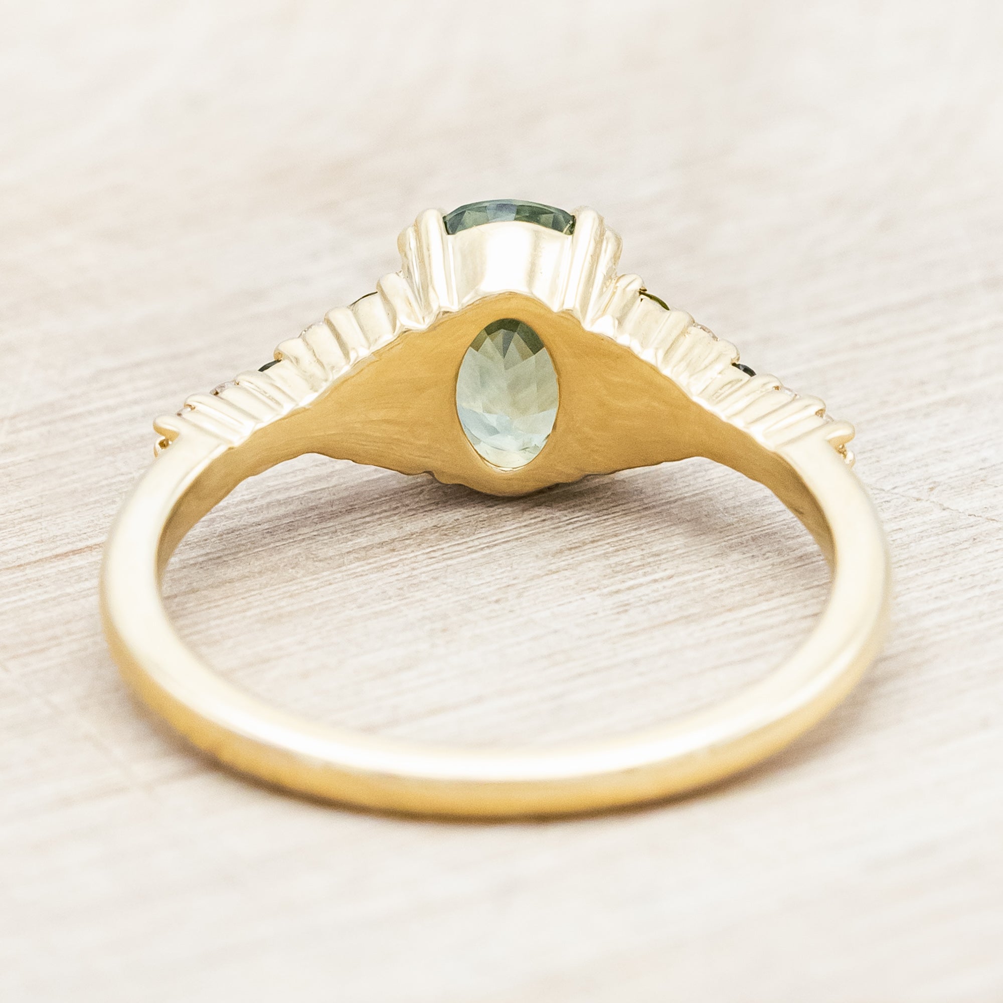 Gold ring with green sapphire and diamond accents on a light wooden surface