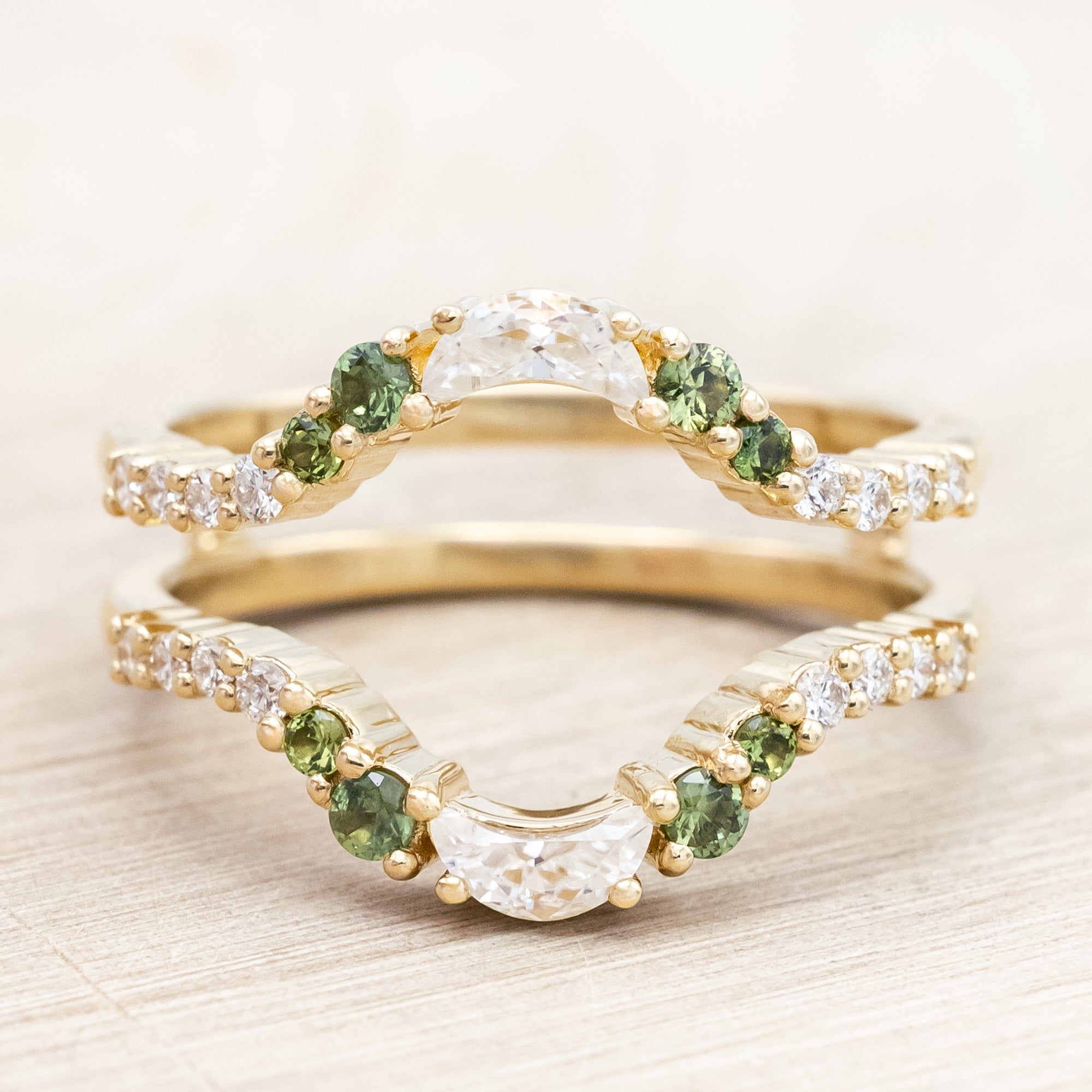 Gold ring with moissanite, green sapphire & diamond accemts on a light wooden surface