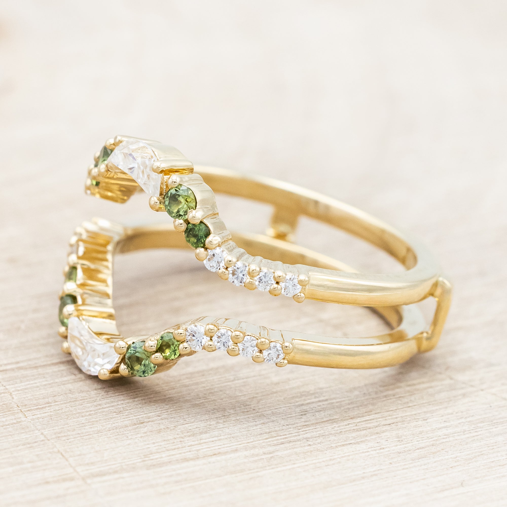 Gold ring with moissanite, green sapphire & diamond accemts on a light wooden surface