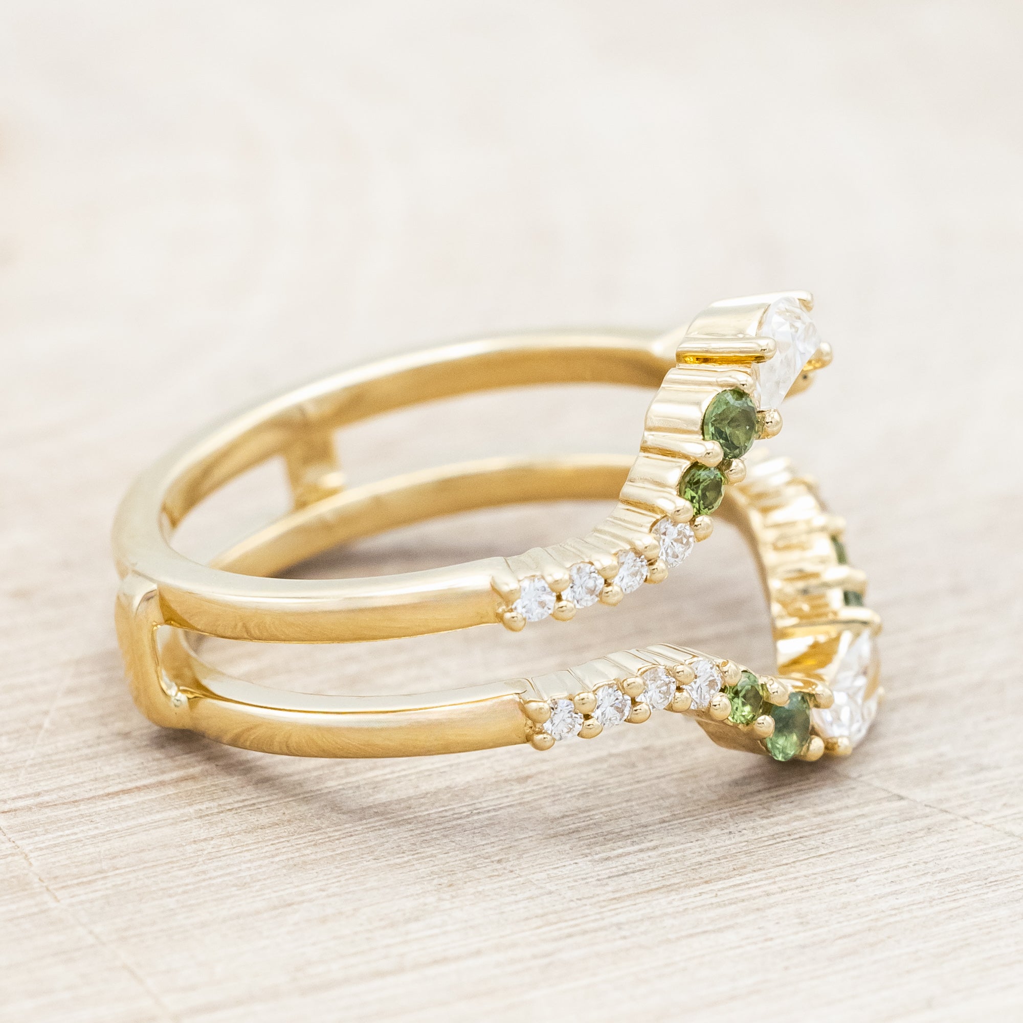 Gold ring with moissanite, green sapphire & diamond accemts on a light wooden surface