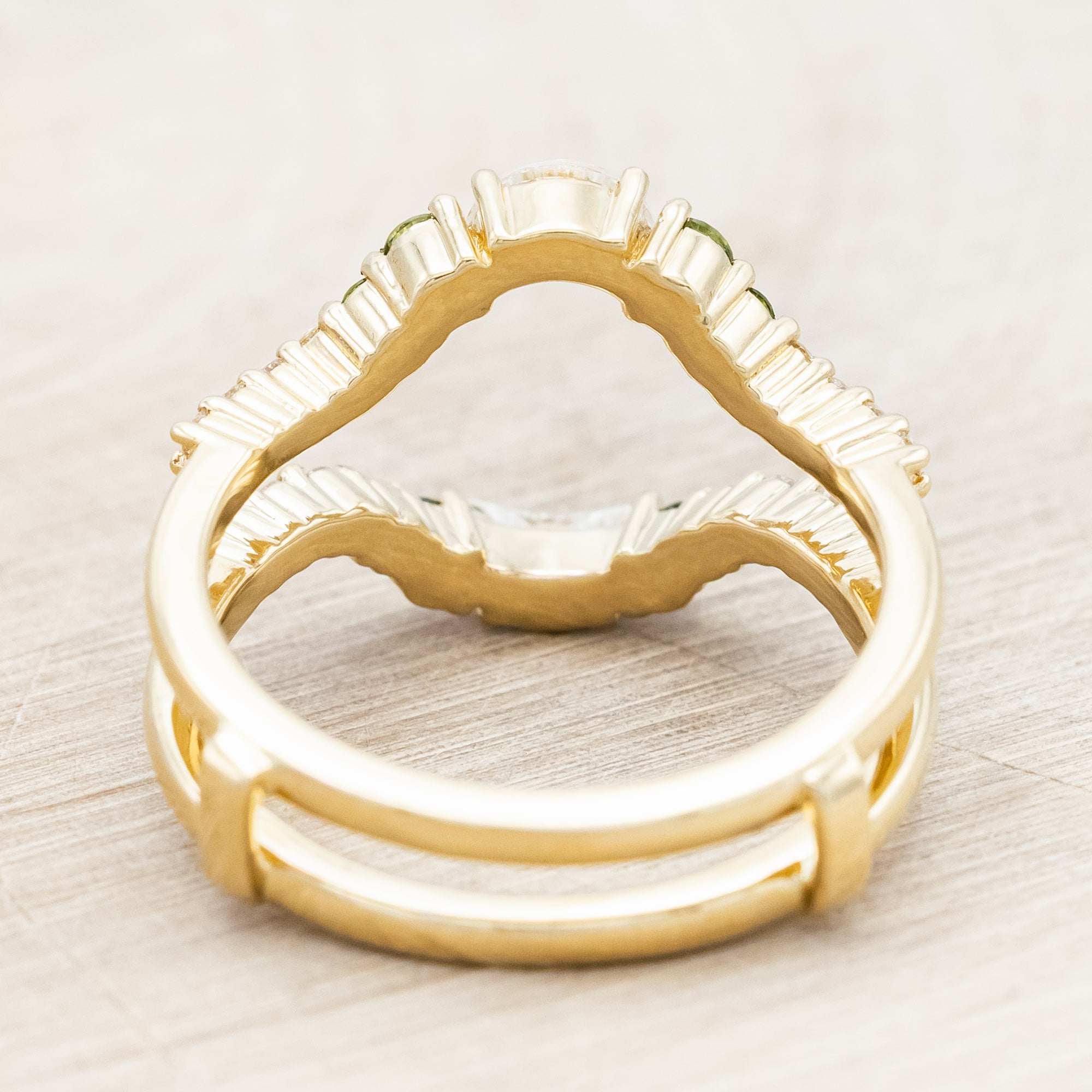 Gold ring with moissanite, green sapphire & diamond accemts on a light wooden surface