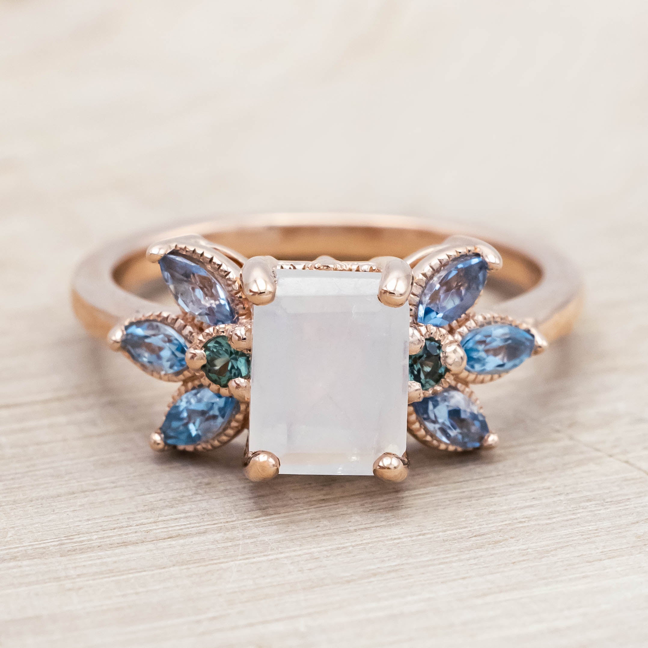 Rose gold ring with a central moonstone surrounded by smaller stones on a neutral background