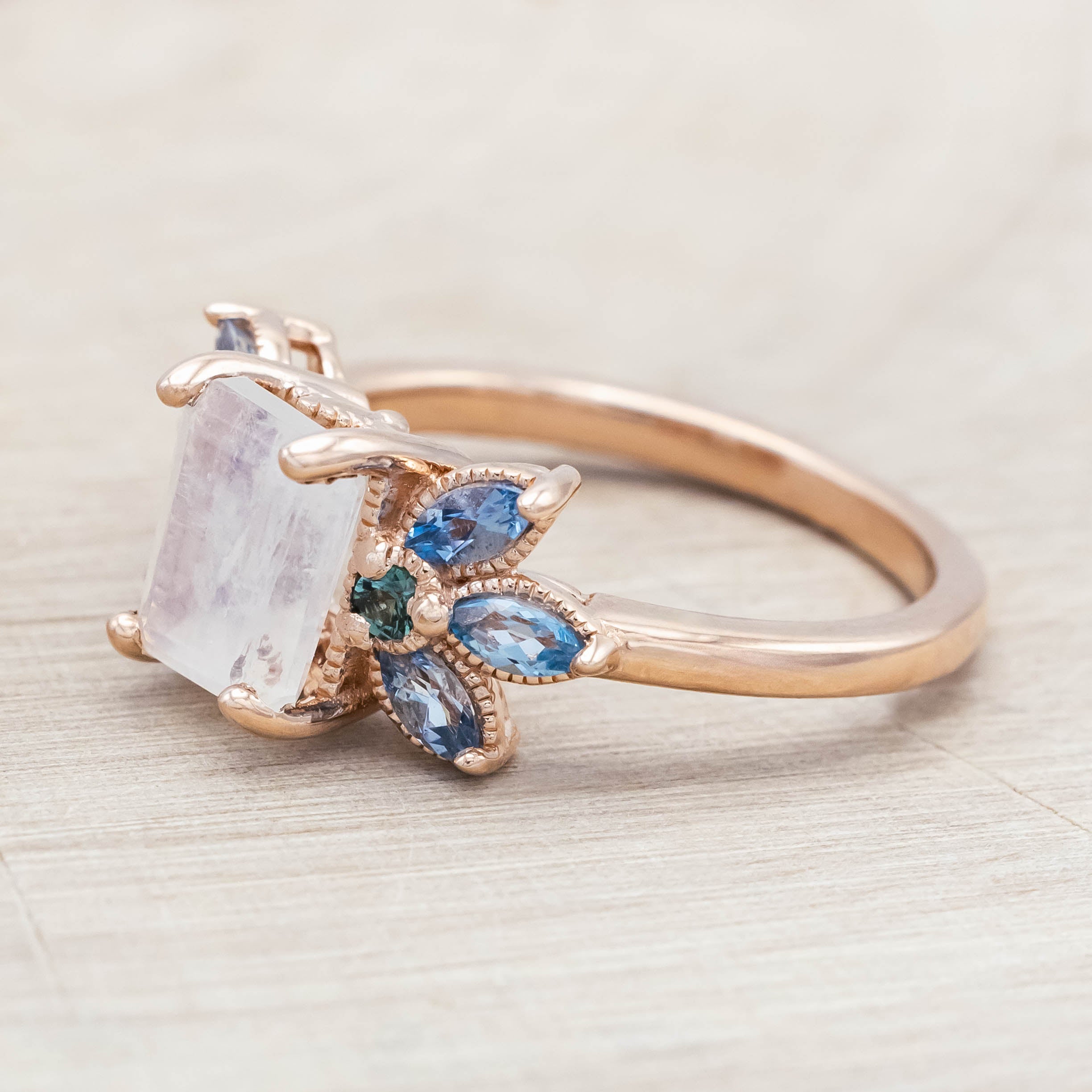 Rose gold ring with a central moonstone surrounded by smaller stones on a neutral background