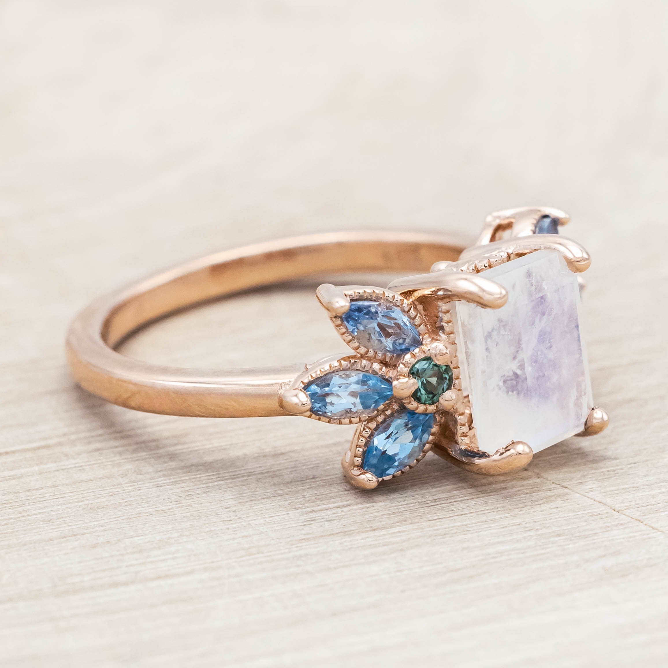 Rose gold ring with a central moonstone surrounded by smaller stones on a neutral background