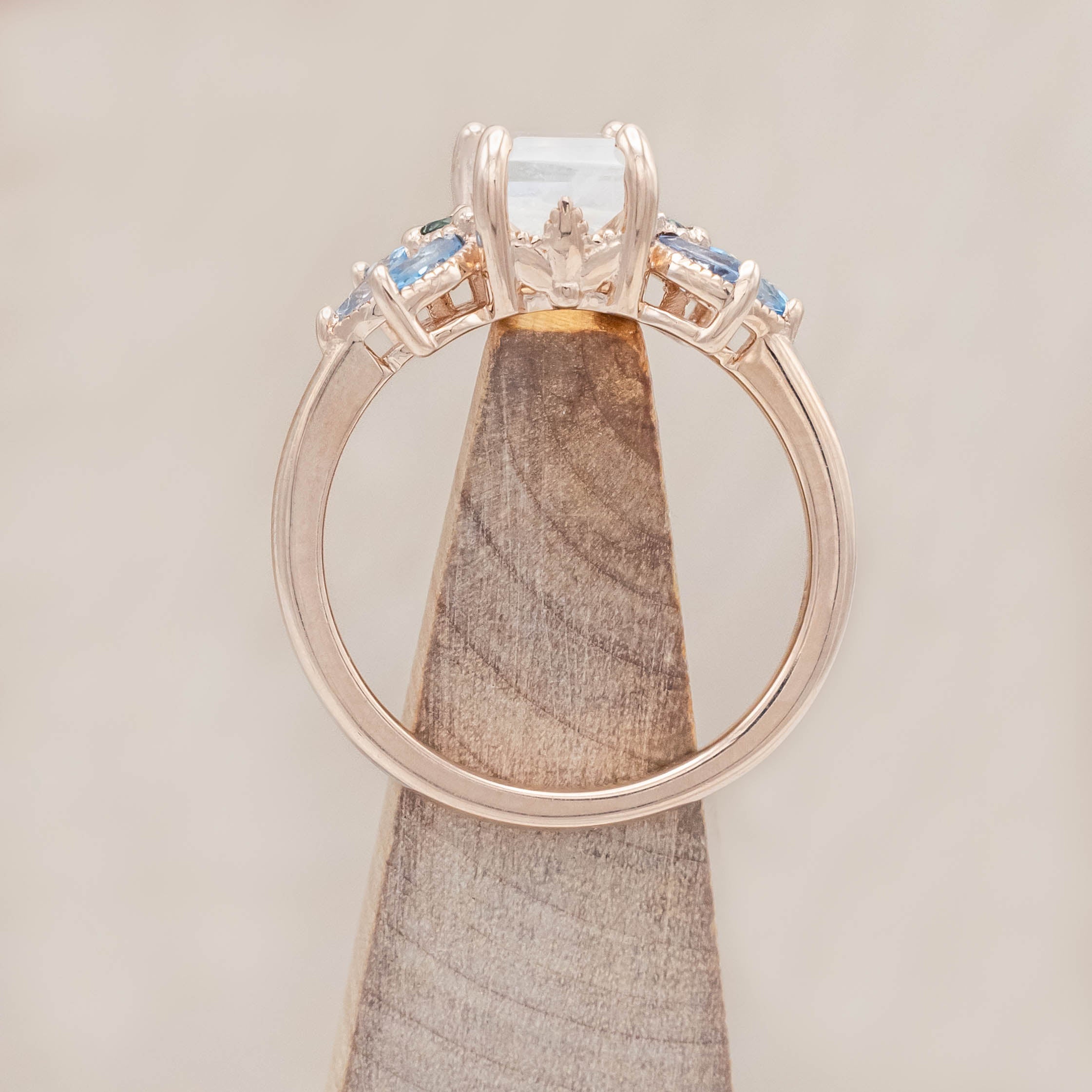 Rose gold ring with a central moonstone surrounded by smaller stones on a neutral background