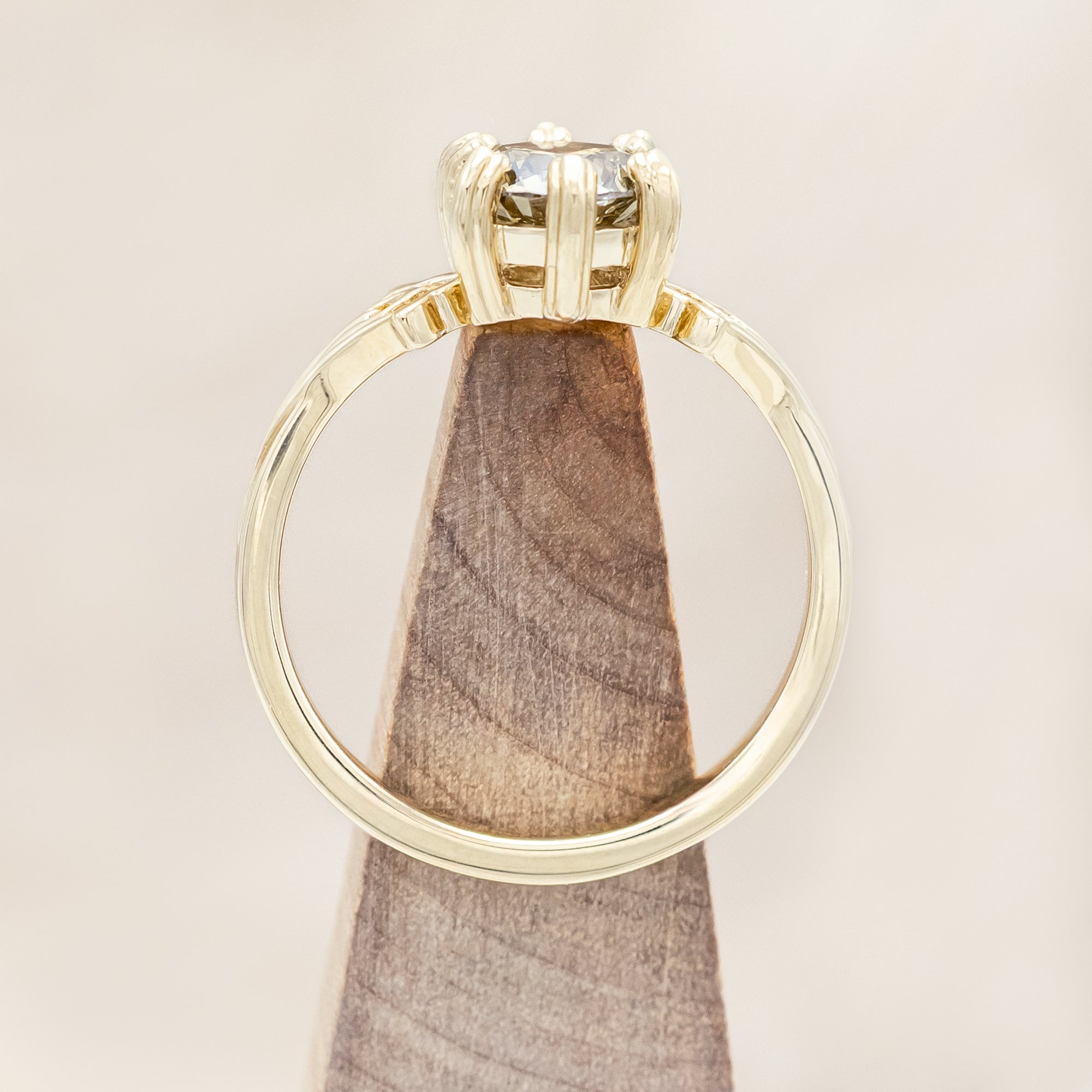 Gold ring with a champagne salt & pepper diamond on a wooden stand against a light wooden surface