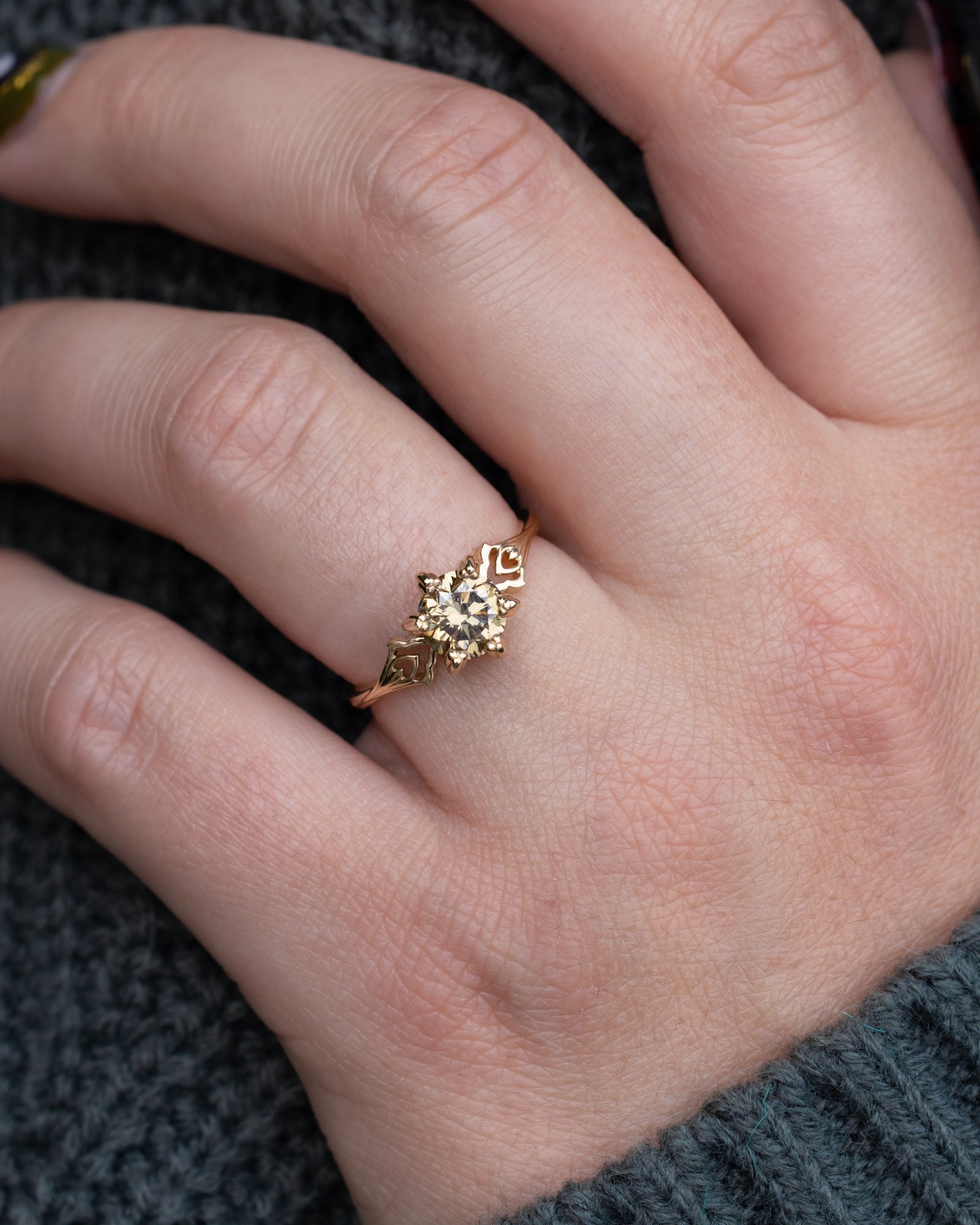 Gold ring with intricate design on a finger against a dark background