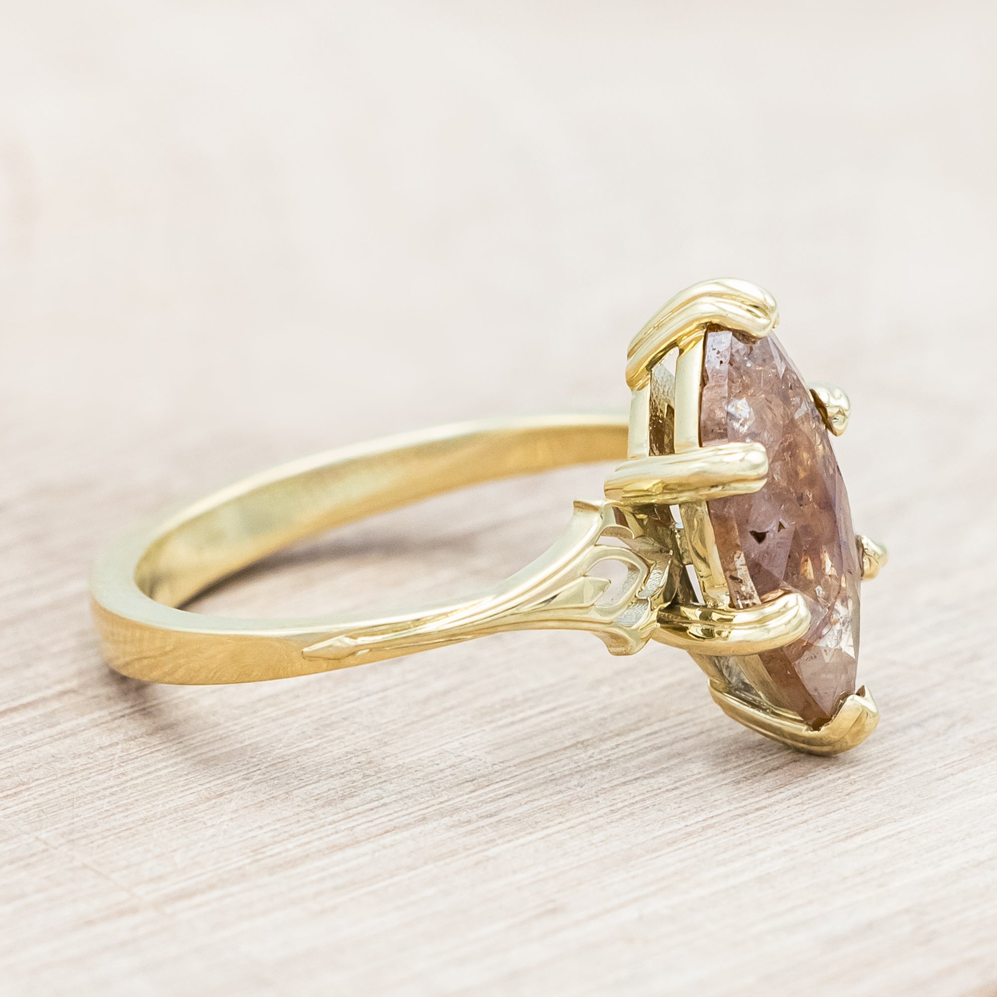 Gold ring with a marquise cut salt & pepper diamond on a light wooden surface