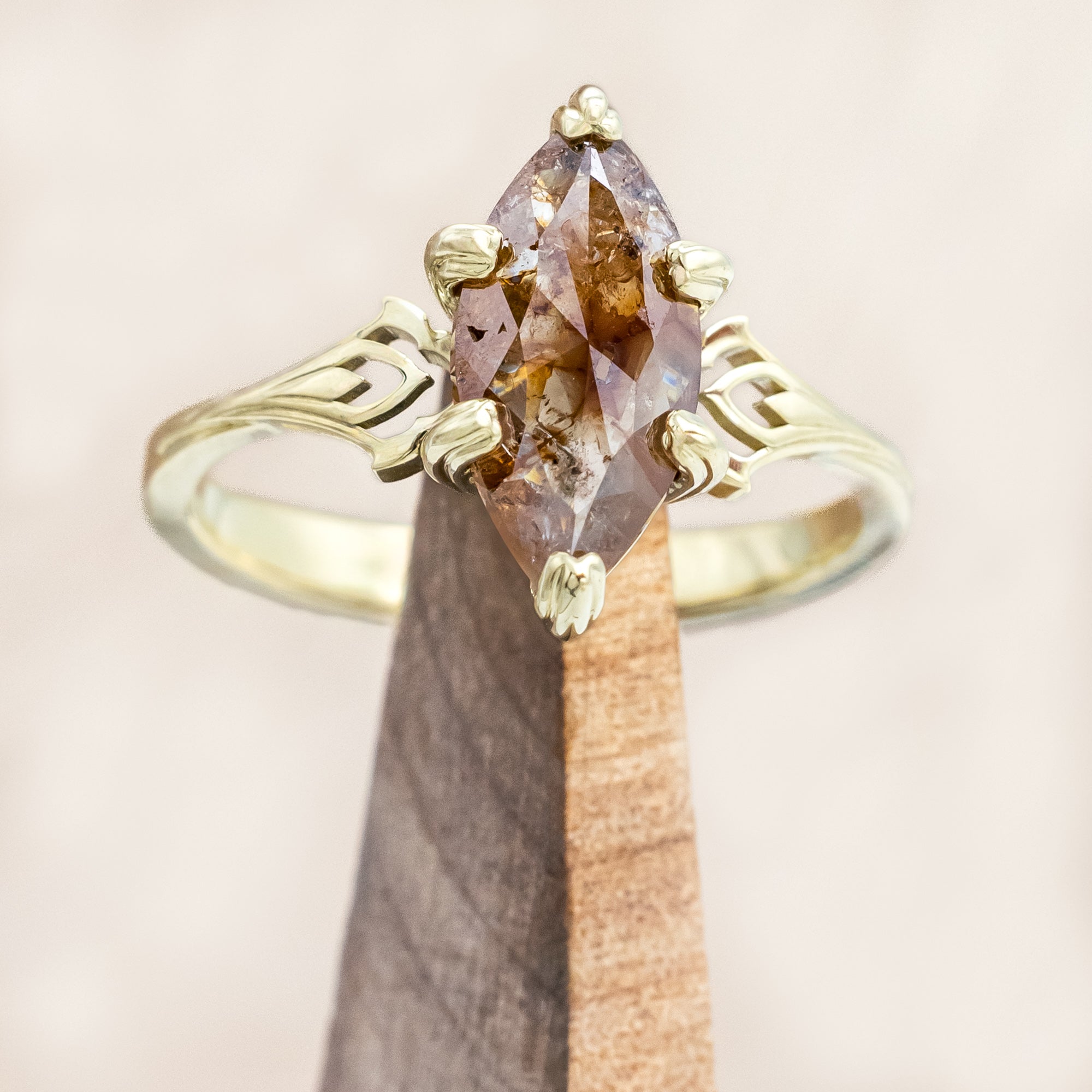 Gold ring with a marquise cut salt & pepper diamond on a wooden stand against a beige background