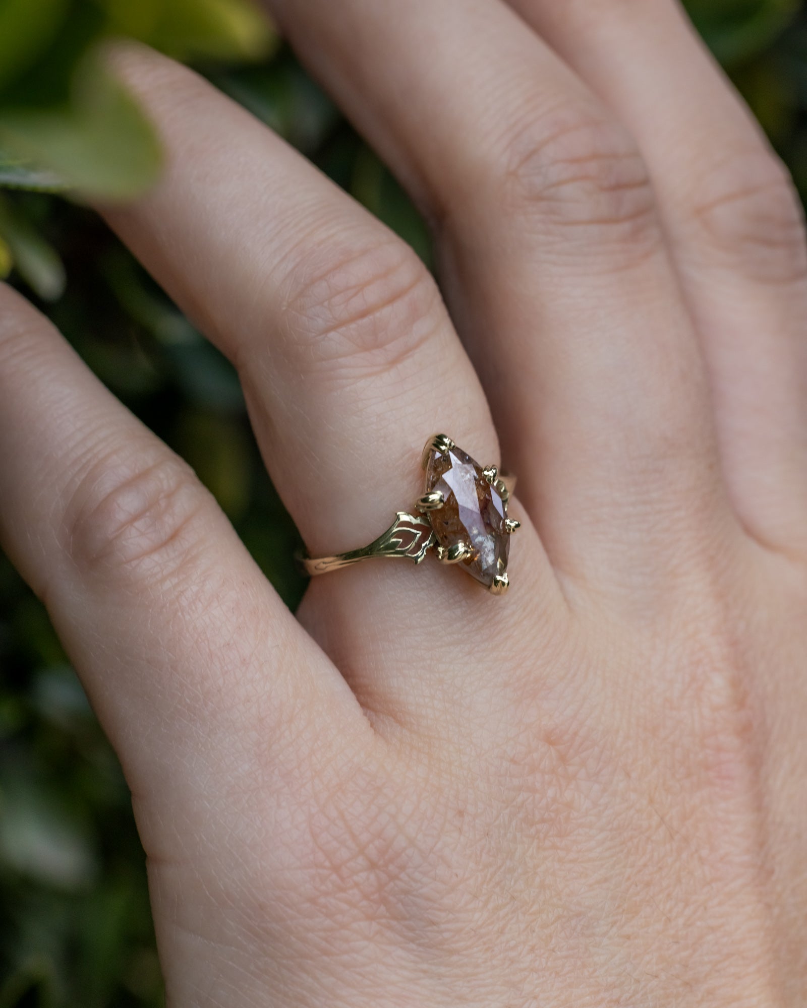 Gold ring with a salt & pepper diamond on a hand against a blurred green background