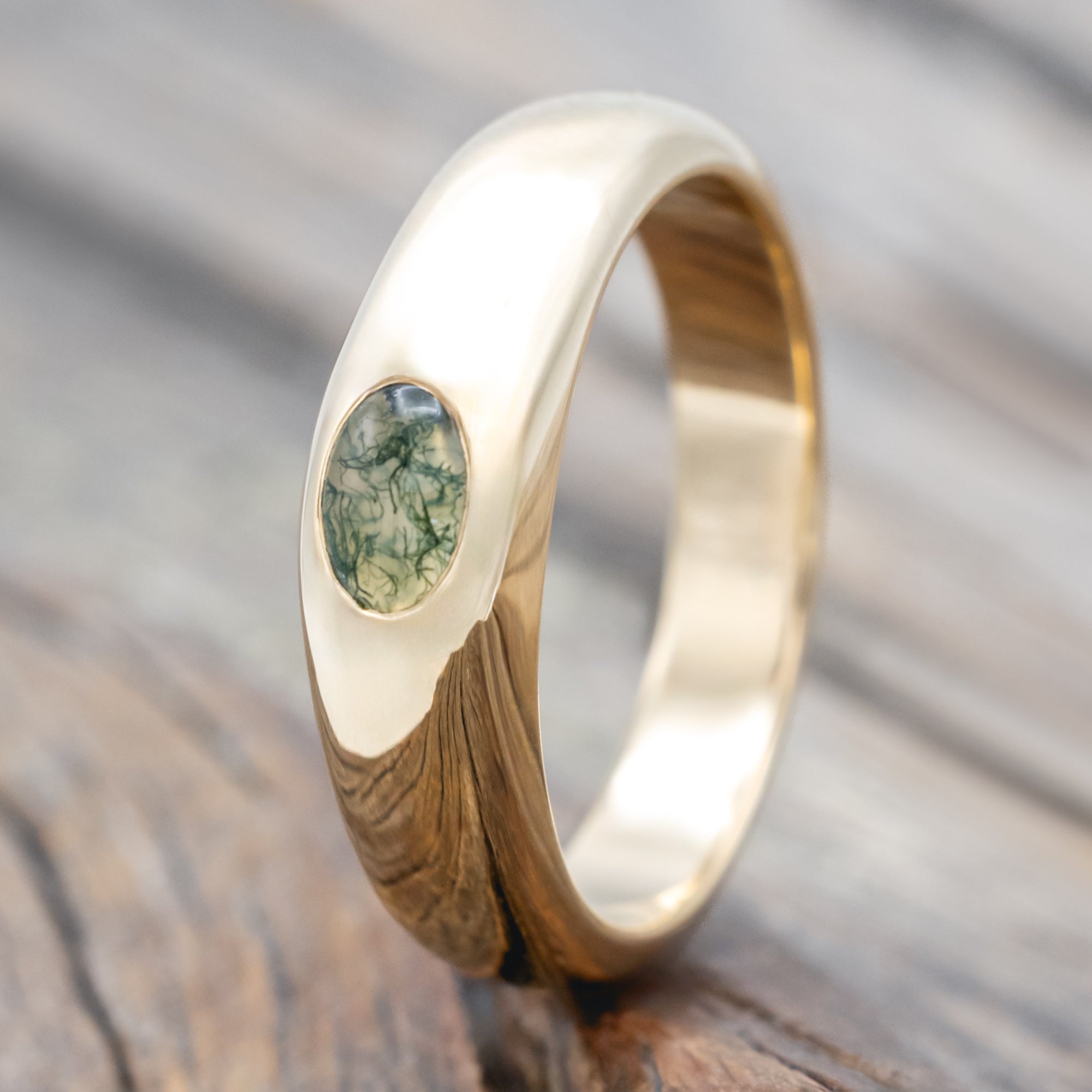 A gold ring with a bezel set moss agate displayed on a wooden surface.