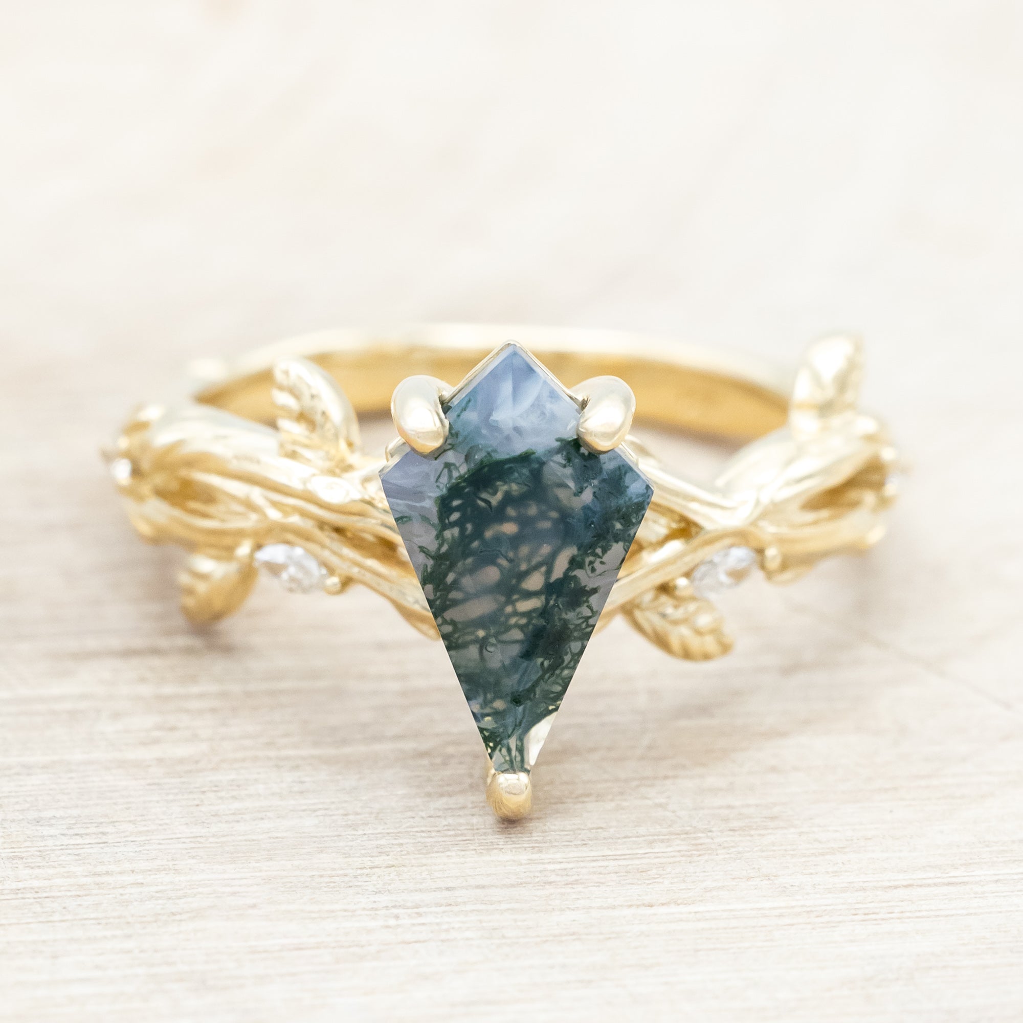 Gold ring with a moss agate with vine-style band and diamond accents on a wooden background