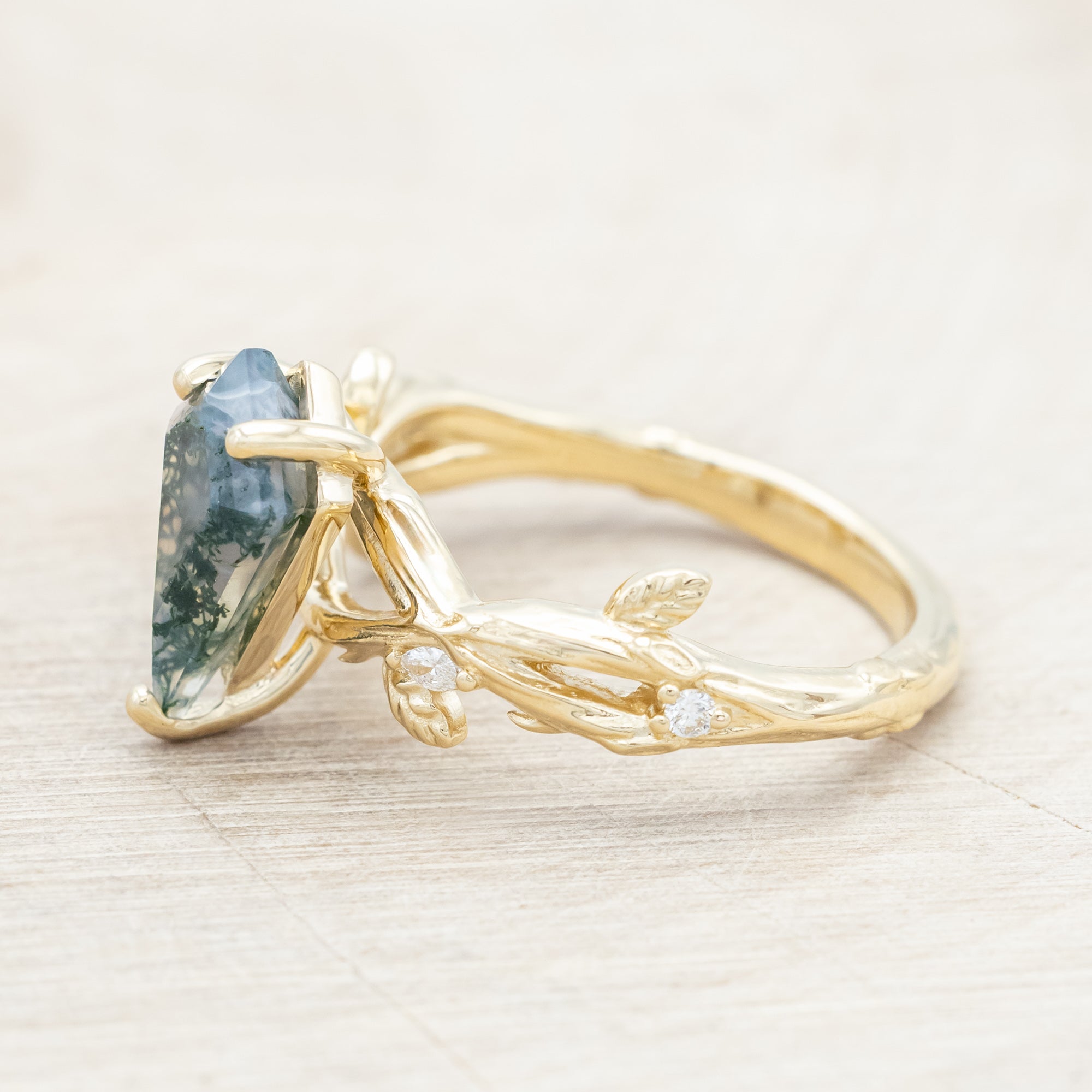 Gold ring with a moss agate with vine-style band and diamond accents on a wooden background