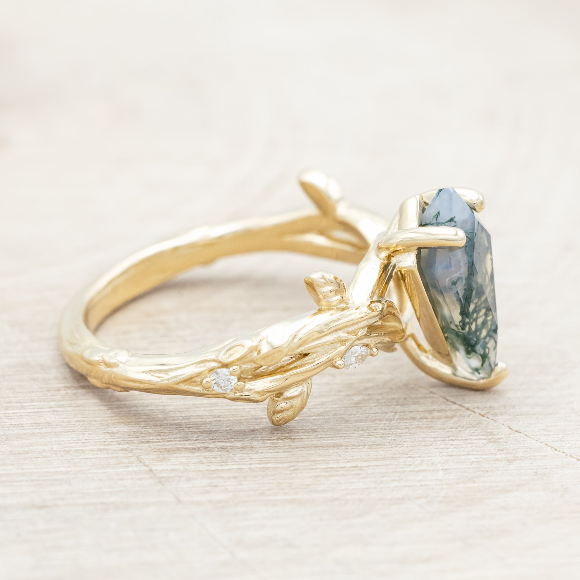 Gold ring with a moss agate with vine-style band and diamond accents on a wooden background