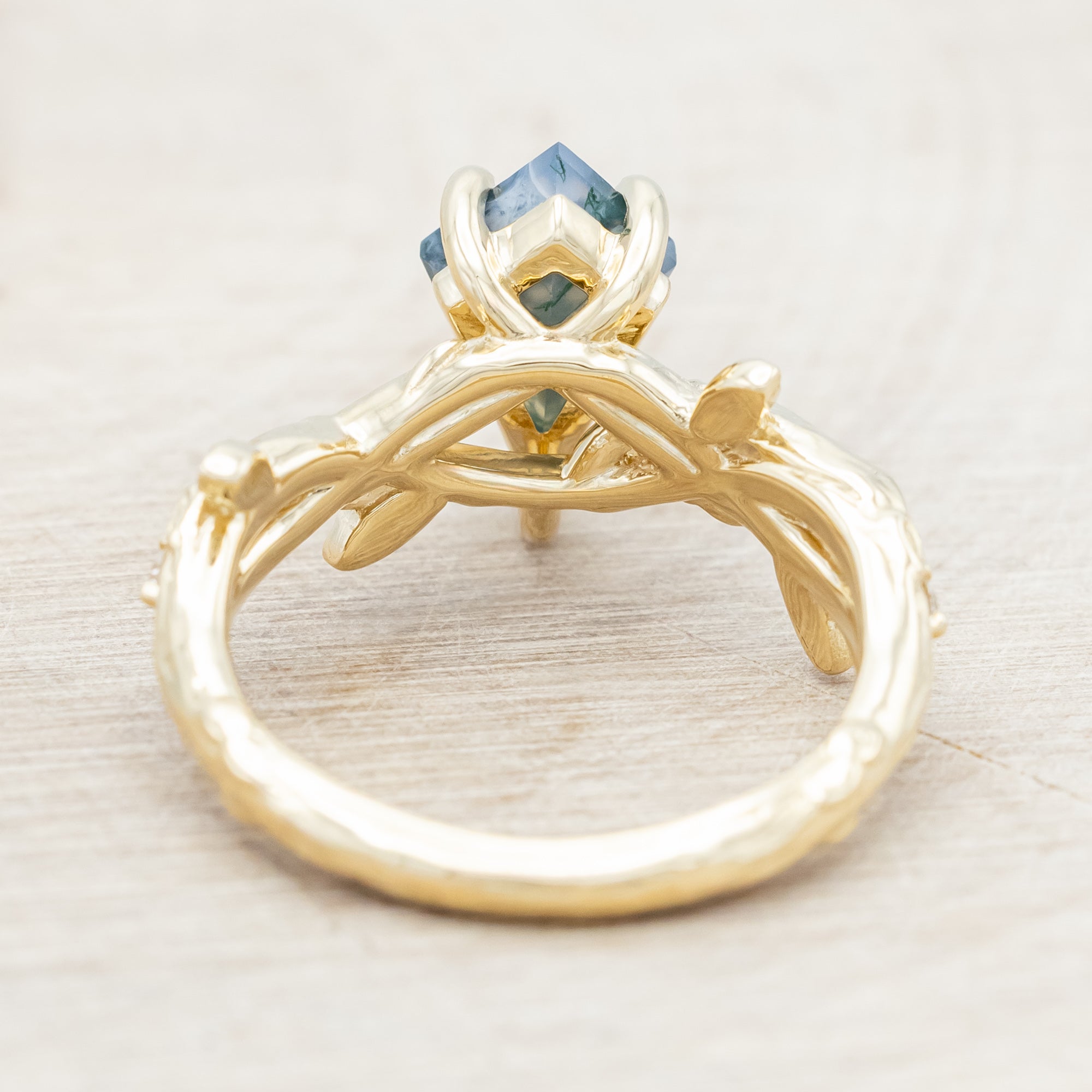 Gold ring with a moss agate with vine-style band and diamond accents on a wooden background