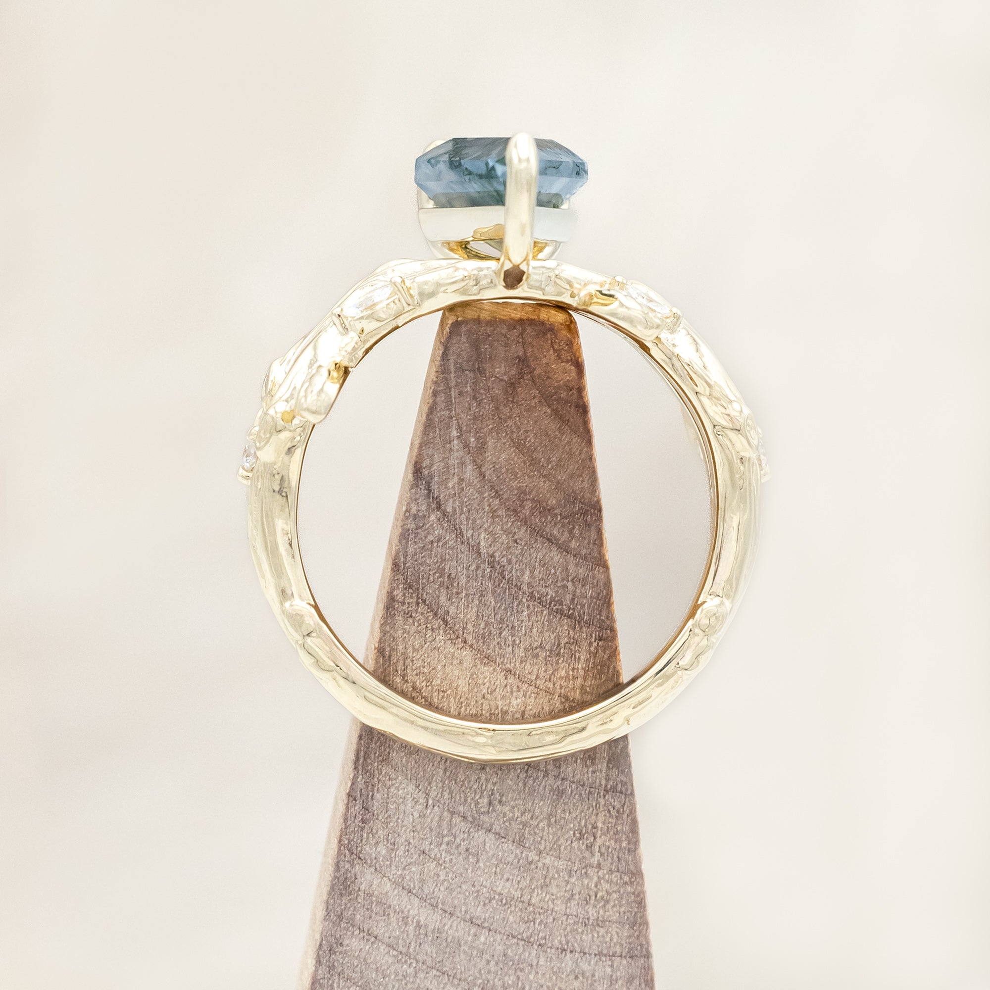 Gold ring with a moss agate with vine-style band and diamond accents on a wooden background